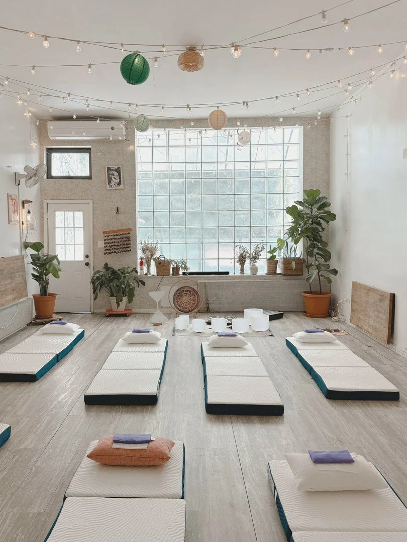 Sound bath studio setup in Brooklyn with floor mattresses, pillows, crystal singing bowls, and soft lighting prepared for a deep rest group session.