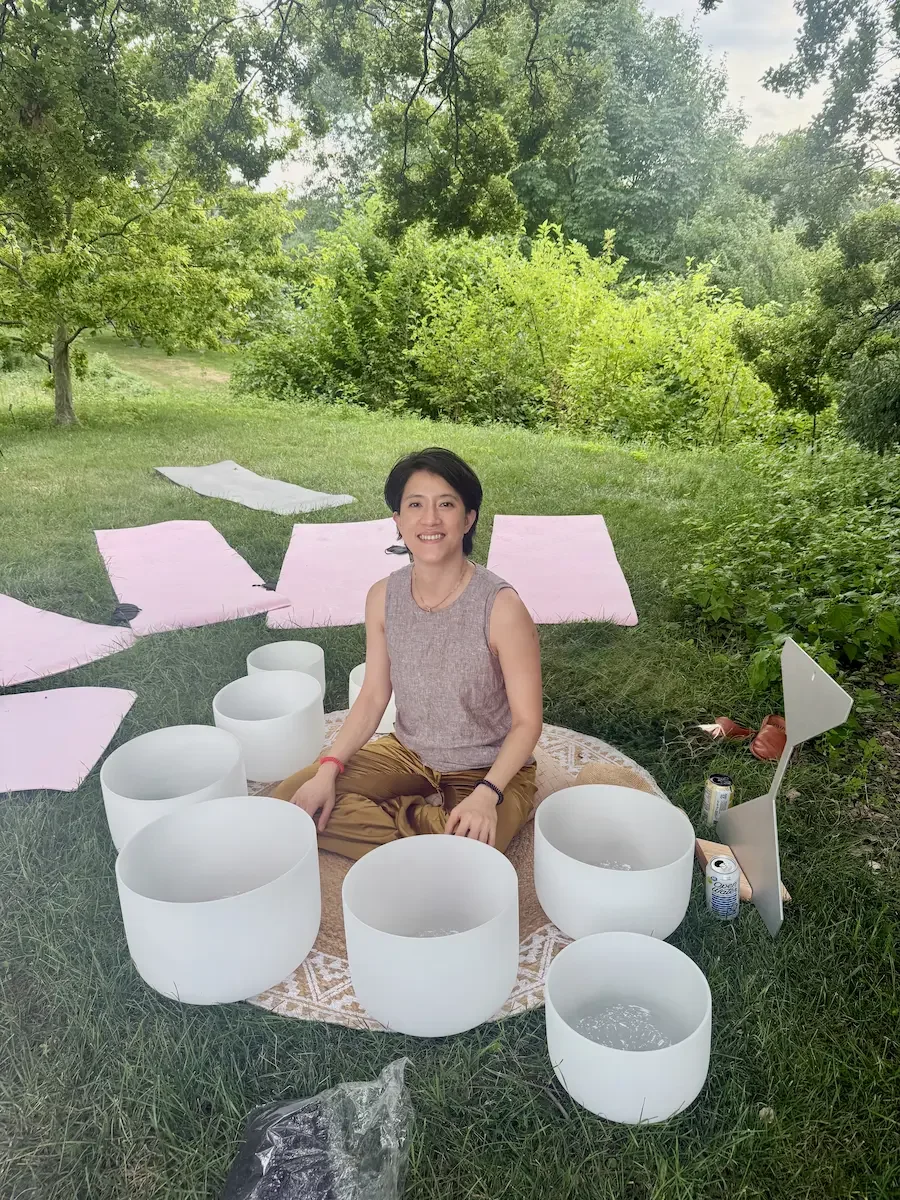 Natalie Chan seated among crystal singing bowls during an outdoor sound bath setup at the New York Botanical Garden for Bloomberg's employee appreciation day