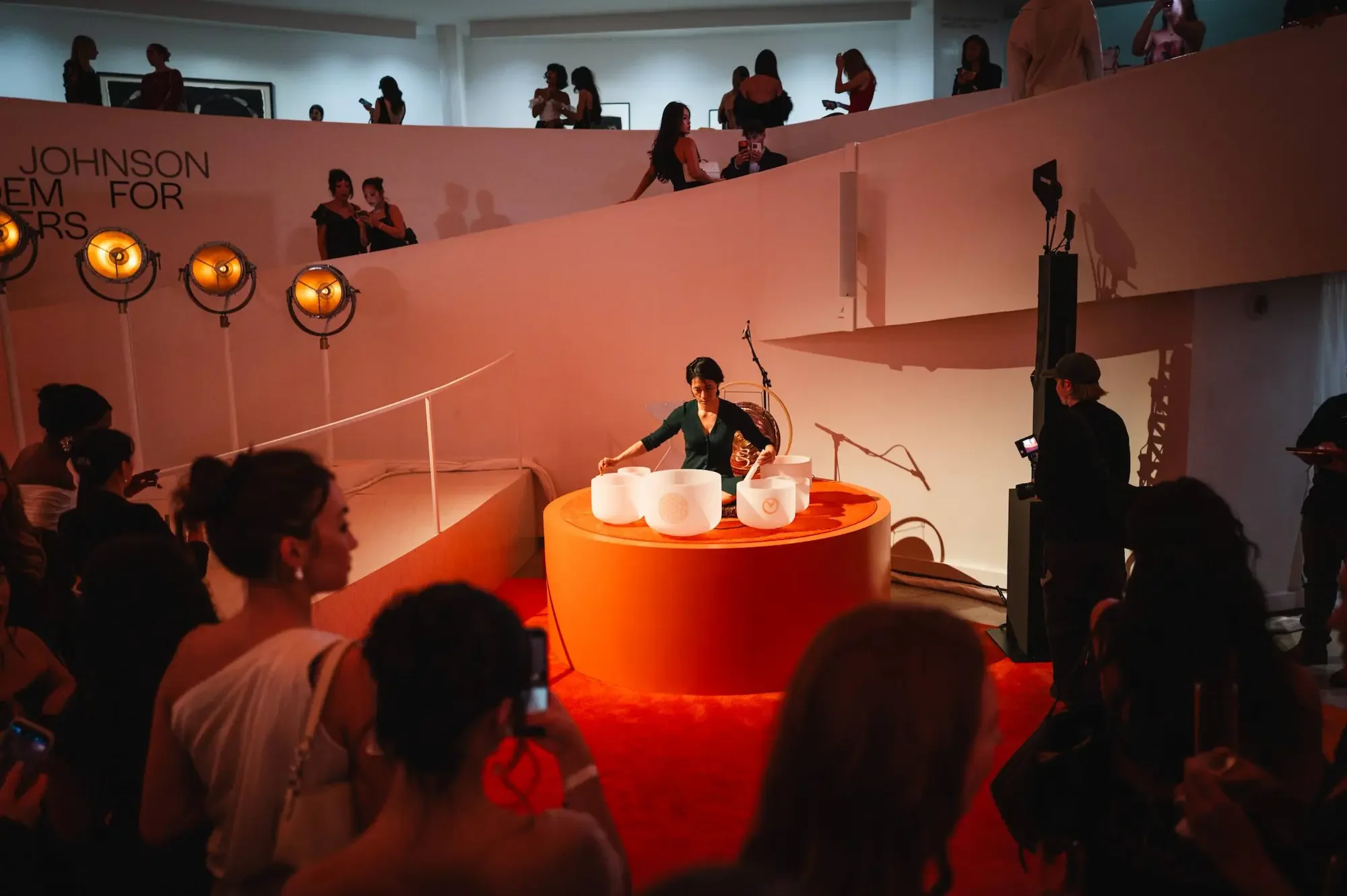 Natalie Chan of Soundawn performing a crystal singing bowl sound ceremony on a lit stage in the Guggenheim rotunda, surrounded by a crowd in New York City