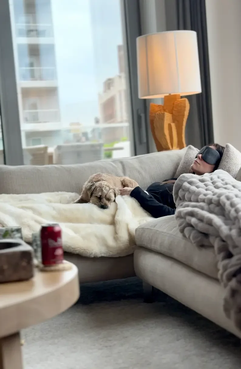 Client relaxing on the couch with an eye mask and her dog during a private virtual sound bath session at home — Soundawn.