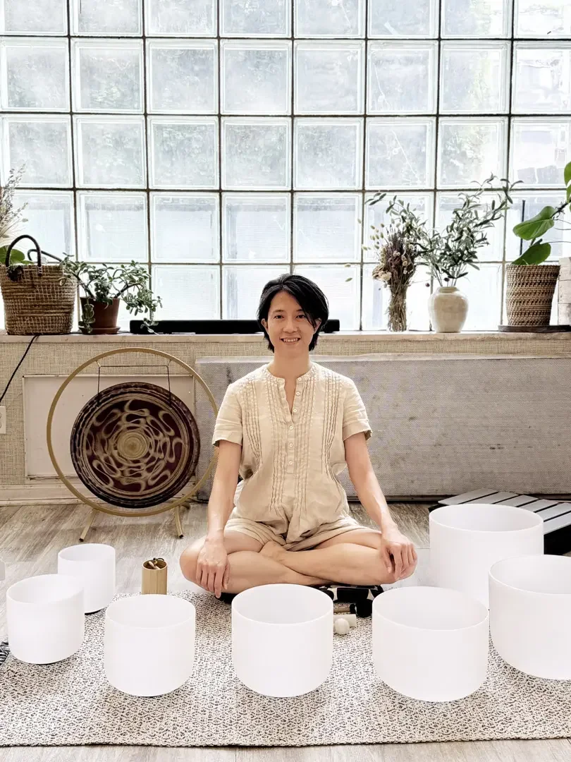 Natalie Chan seated with crystal singing bowls and gong in her Brooklyn studio, preparing to guide a private deep rest sound bath session.