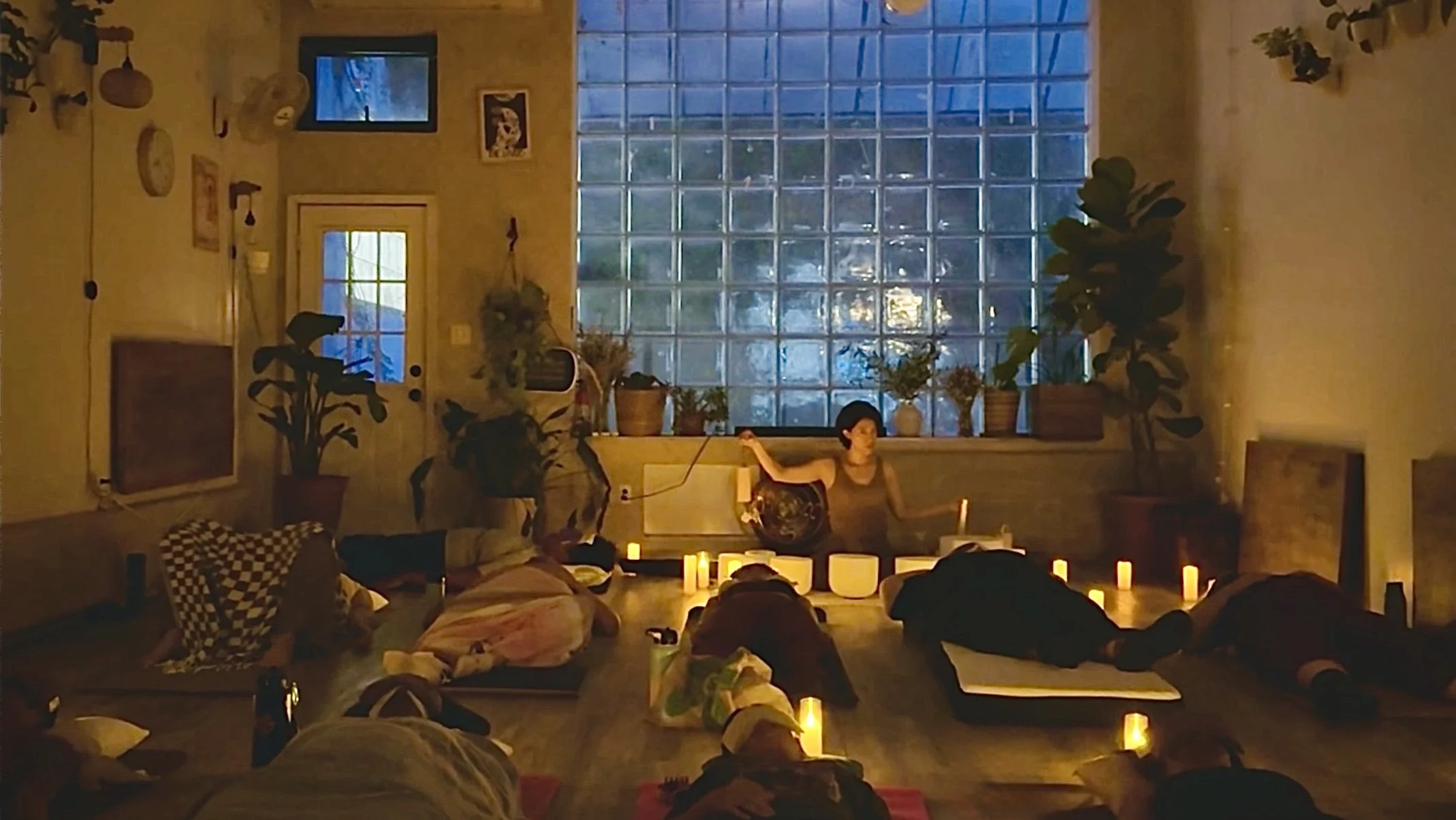 Candlelit sound bath and movement session in Brooklyn led by Natalie Chan, with participants resting on yoga mats surrounded by warm candlelight and plants.