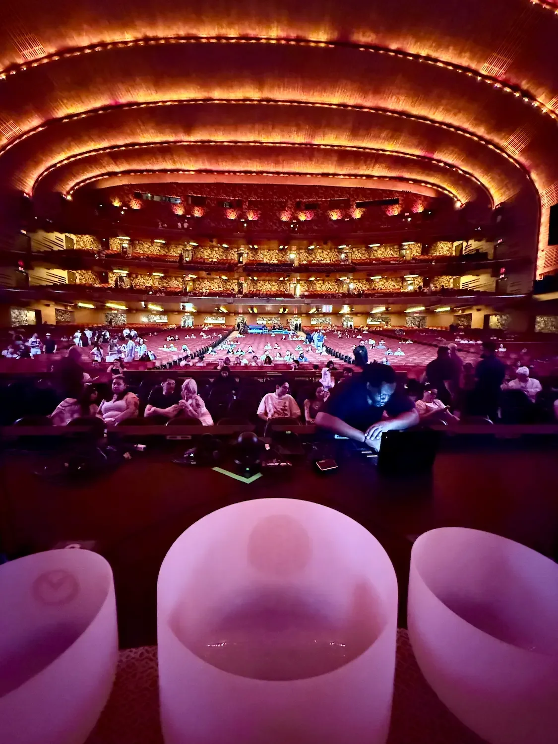 Crystal sound bowls on the Radio City Music Hall stage with the golden auditorium and audience behind — Soundawn's Natalie Chan performing in New York City.