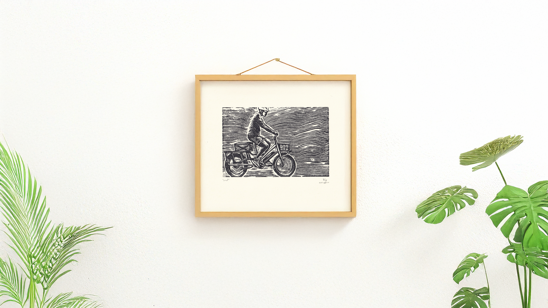 A framed version of a one-color linocut print of a person riding an electric bike with a basket on the front of the bike. Black ink print. Denver Colorado. Printed by Andrew Alger