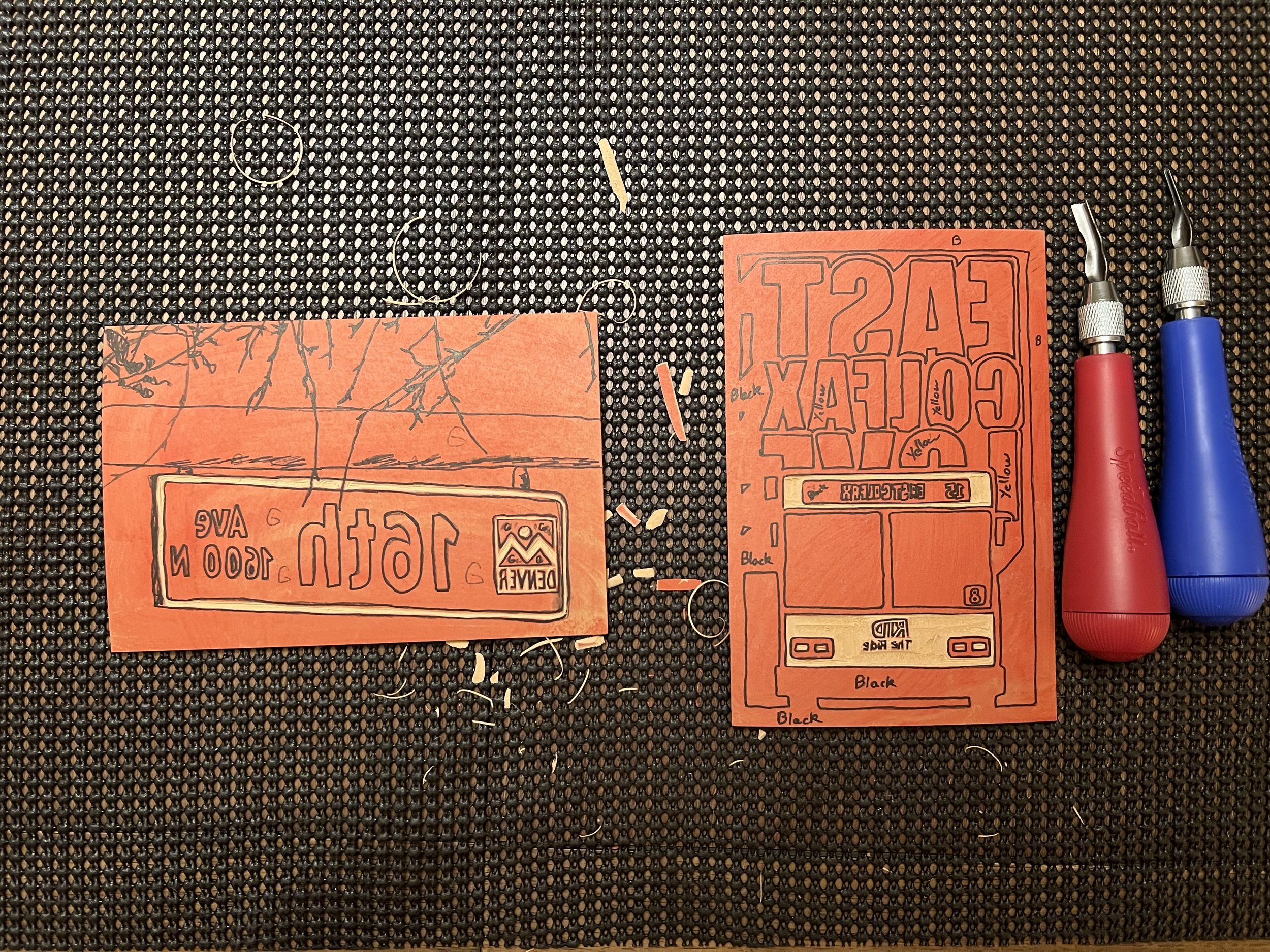 Linocut blocks in the process. Carving tools to the side and scraps of linocuts scattered about.
