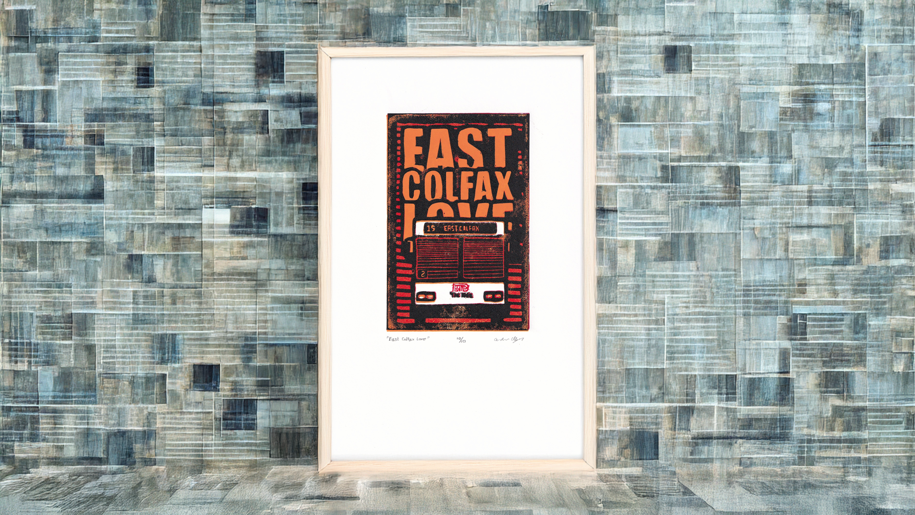 A framed version of linocut print titled "East Colfax Love" with the front of the 15 RTD bus in Denver, Colorado. The print is black, red, orange and white.