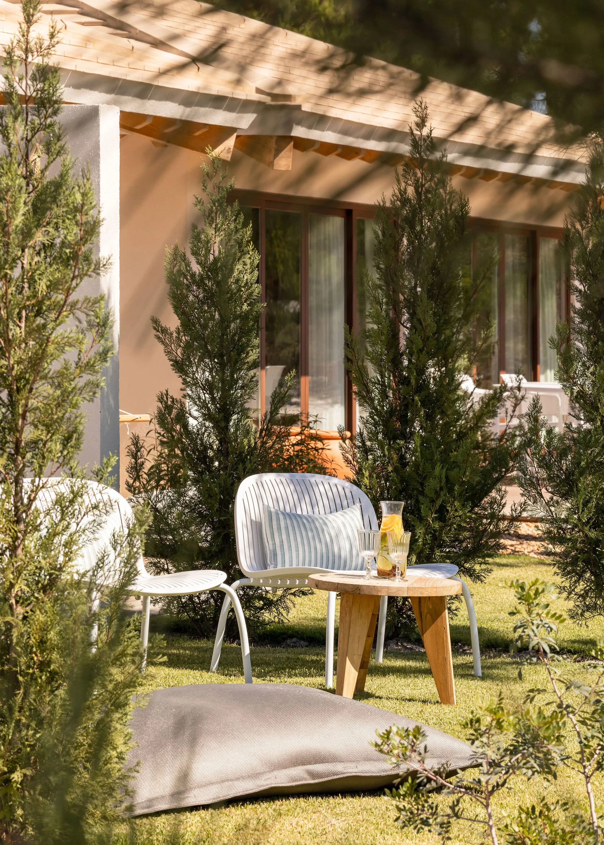 Quarto com teto de madeira, varanda aberta com vista para árvores, cortinas, mobiliário de madeira e uma rede na varanda.