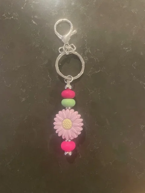Pink and green daisy charm keychain with pink beads on a gray surface.
