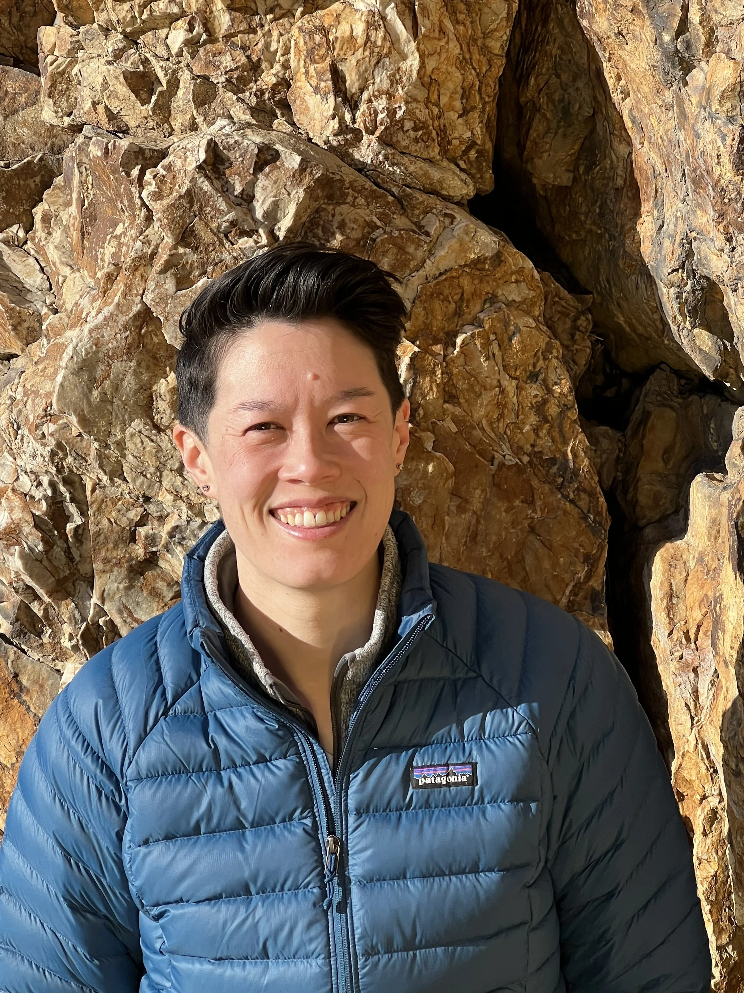 Smiling man in a blue Patagonia jacket taking a selfie in front of a rocky cave opening
