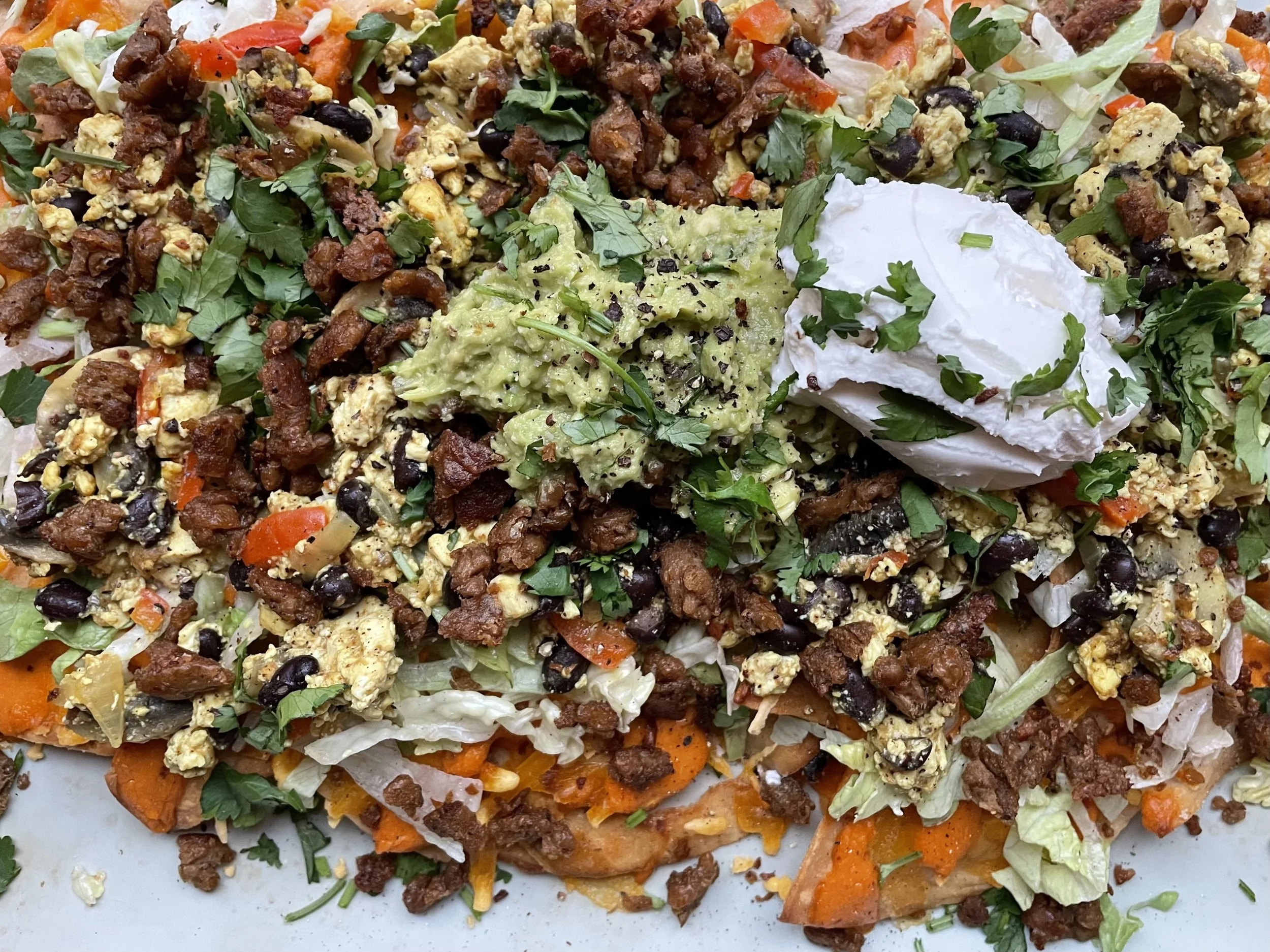 southwest tofu scramble breakfast nachos with vegan cheese sauce, meatless sausage crumbles, black beans, red bell pepper, avocado, and dairy-free sour cream - meatless and wheatless recipe