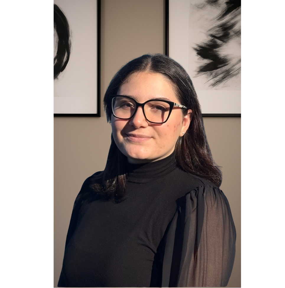 A non-profit accountant with shoulder-length black hair, wearing glasses and a black top with sheer sleeves, standing in front of abstract black-and-white artwork on a beige wall.