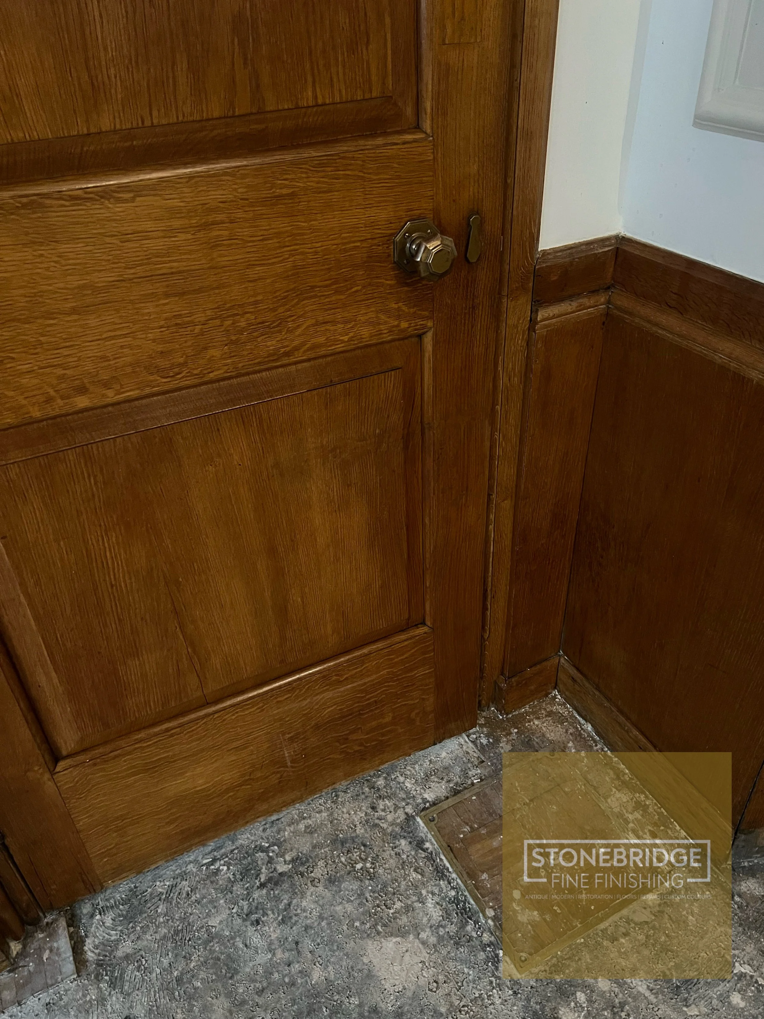 Close-up of a wooden cabinet with a door latch, situated above a rough, unfinished floor.