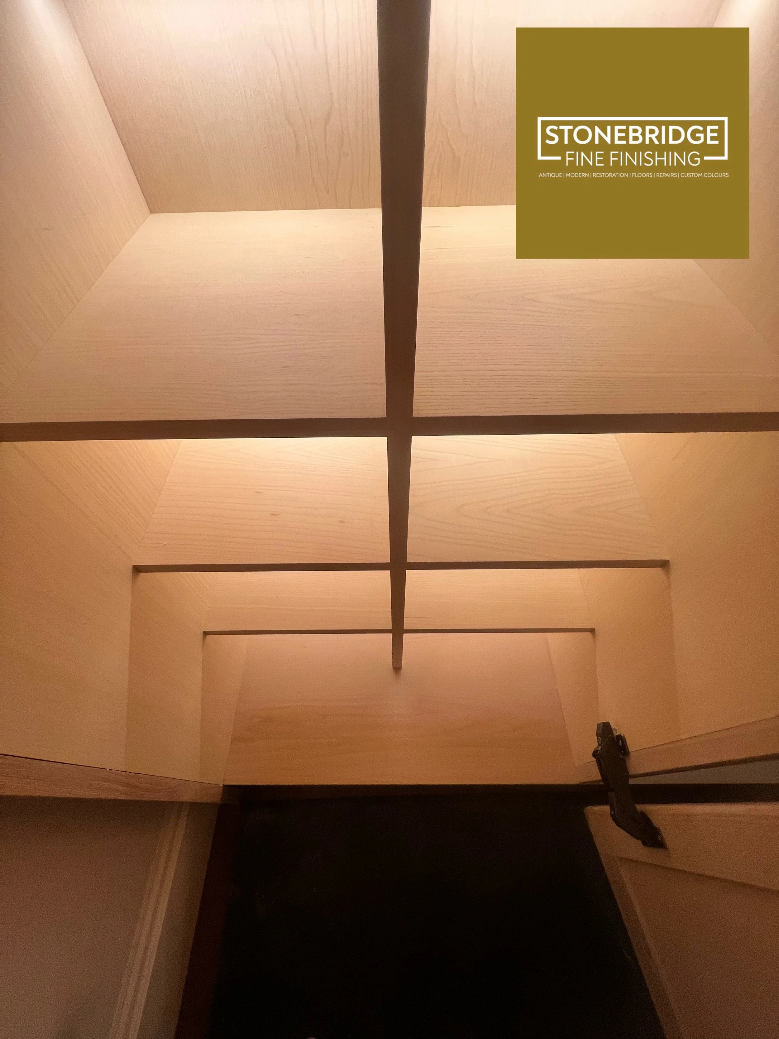 View from inside an elevator shaft showing a wooden structure with cross beams and a door at the bottom, with a logo for Stonebridge Fine Finishing in the upper right corner.