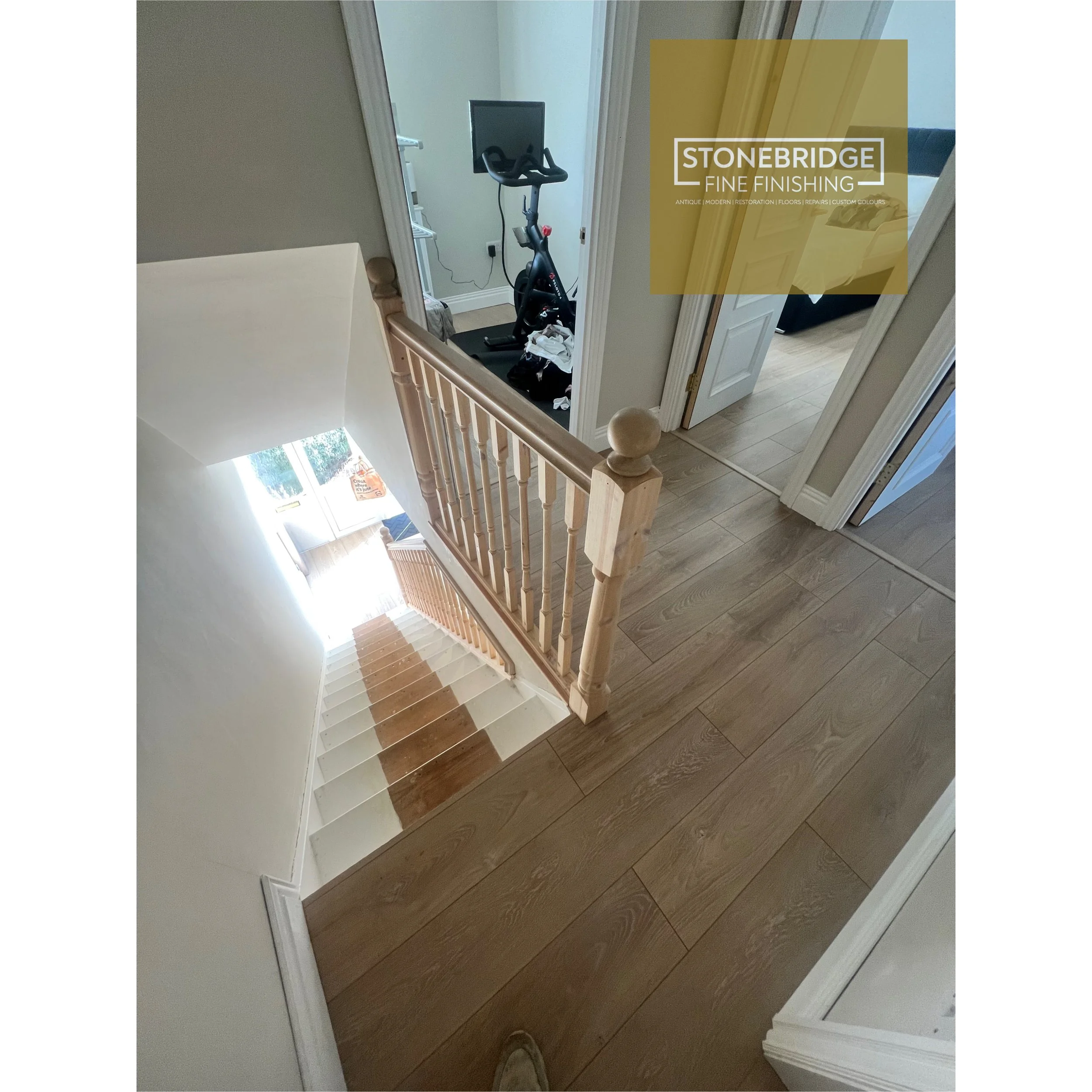 View of a staircase with wooden steps and beige walls, showing an exercise bike in a small room at the top of the stairs.