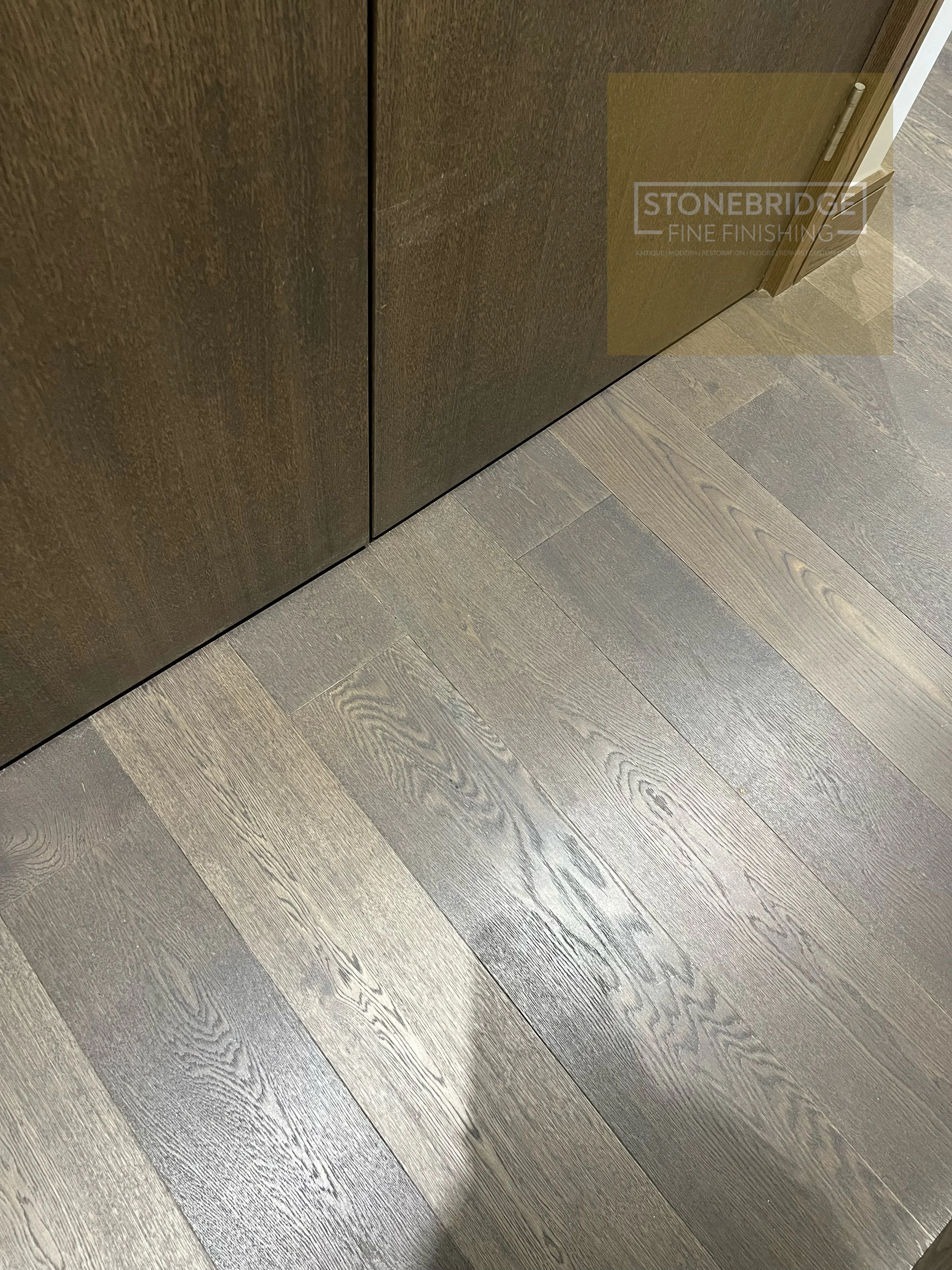 Close-up of a section of dark wood flooring and a piece of dark brown textured cabinetry with a hinge visible at the edge.