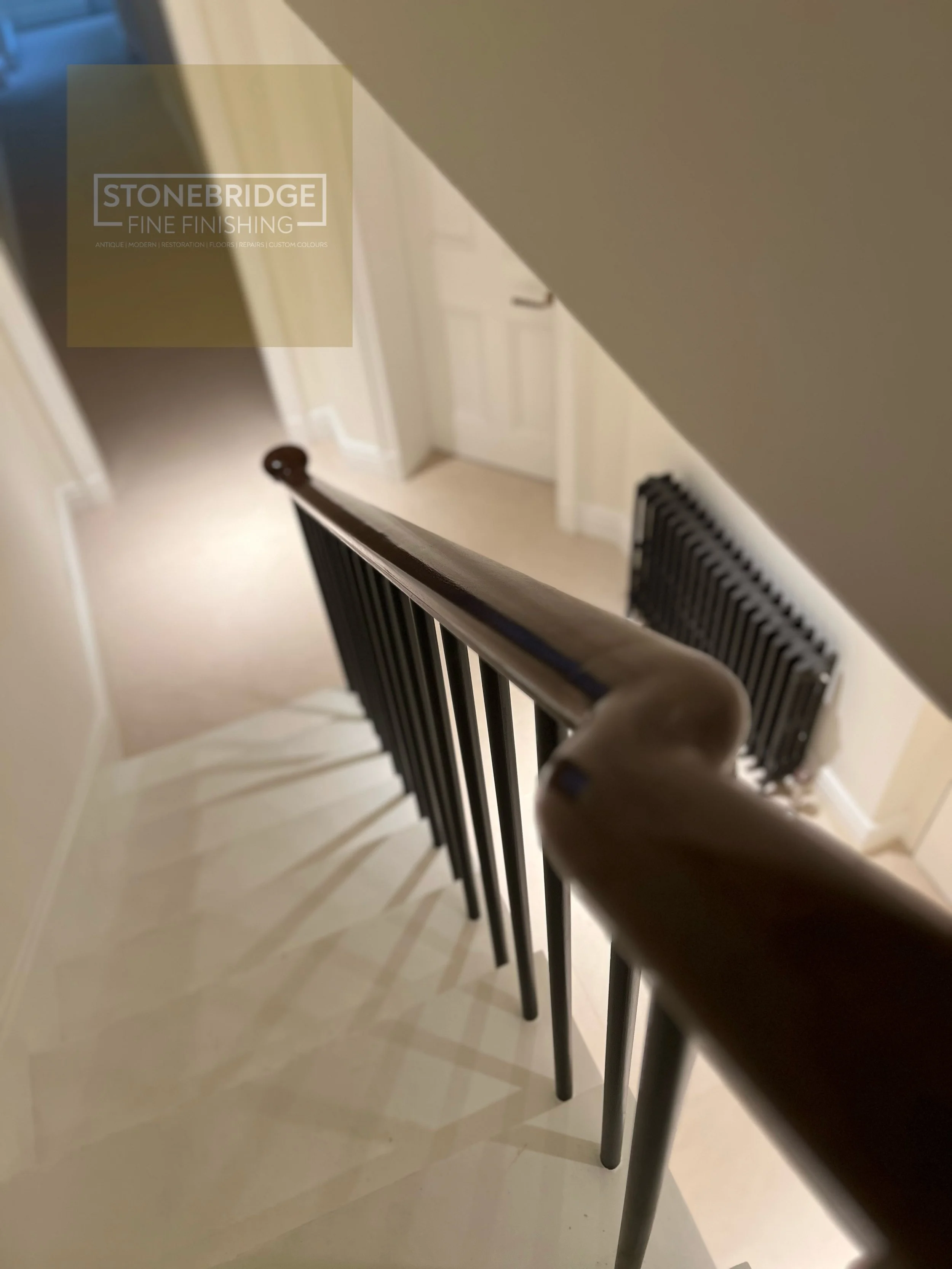 View from the top of a staircase looking down, showing black metal railings and beige walls and floor.