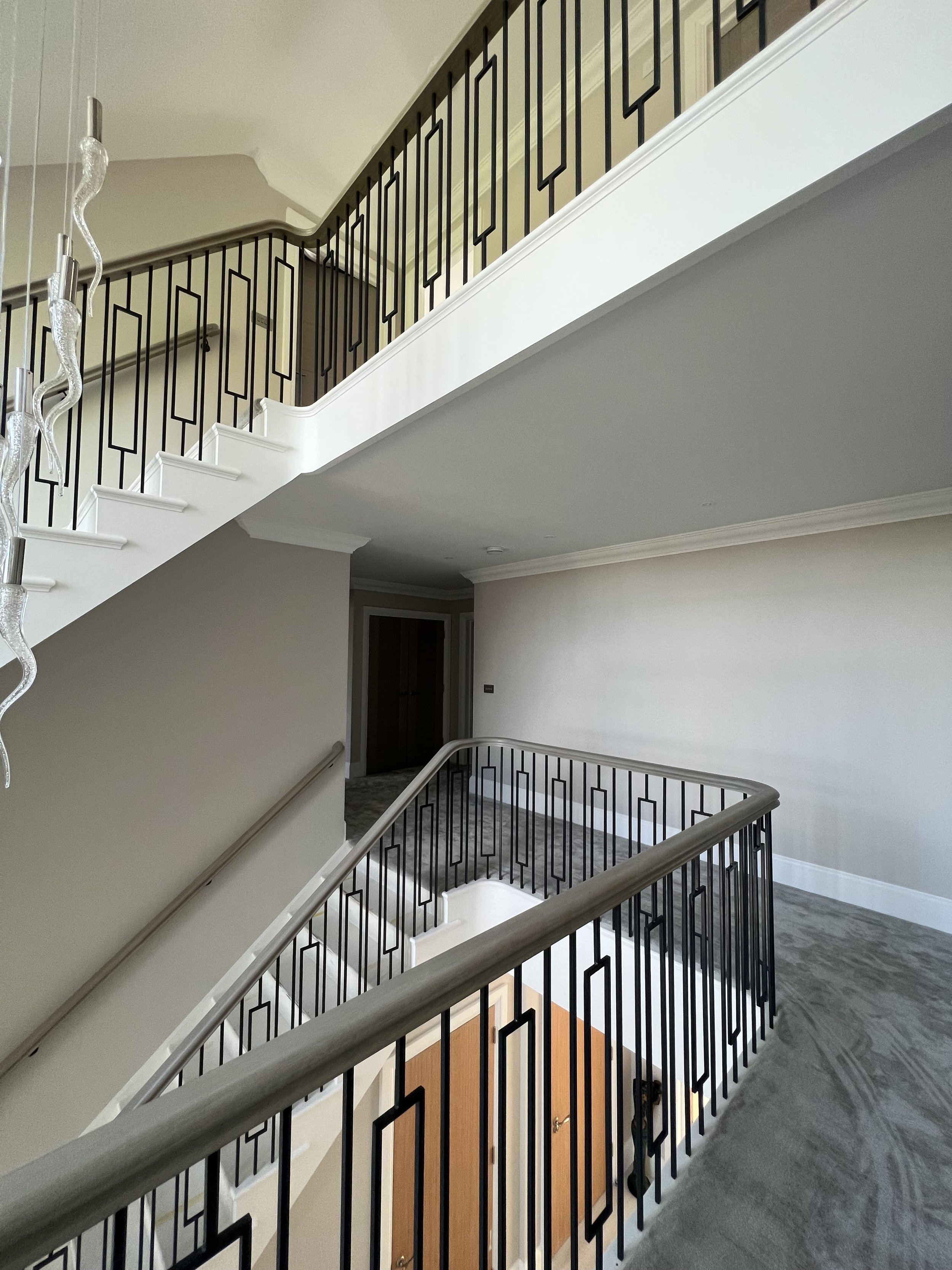 Interior staircase with modern black metal railing, upper and lower levels, and decorative lighting fixture.