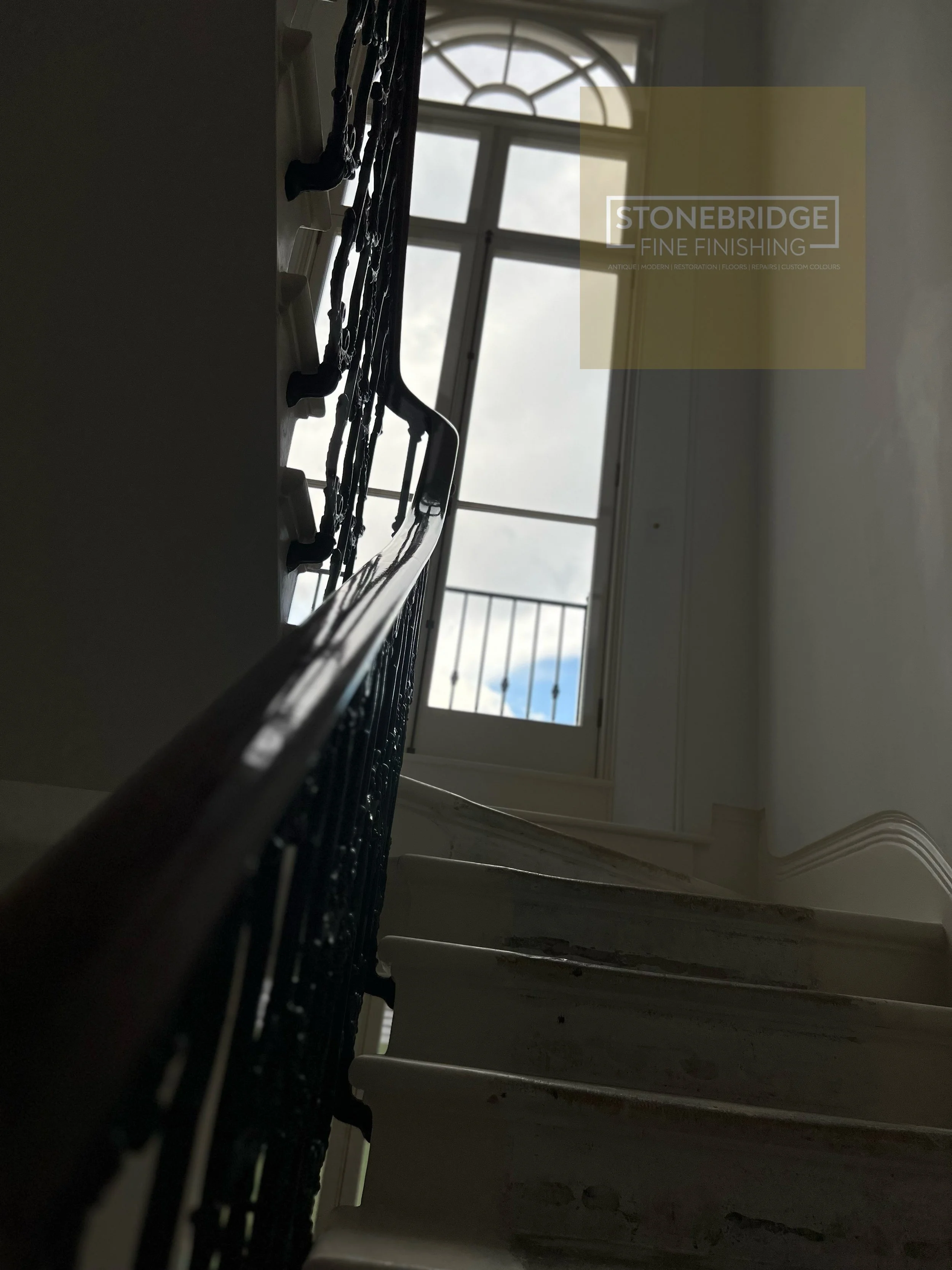 Looking up a staircase towards a window with an arch, bright sky visible outside, with a railing on the staircase.