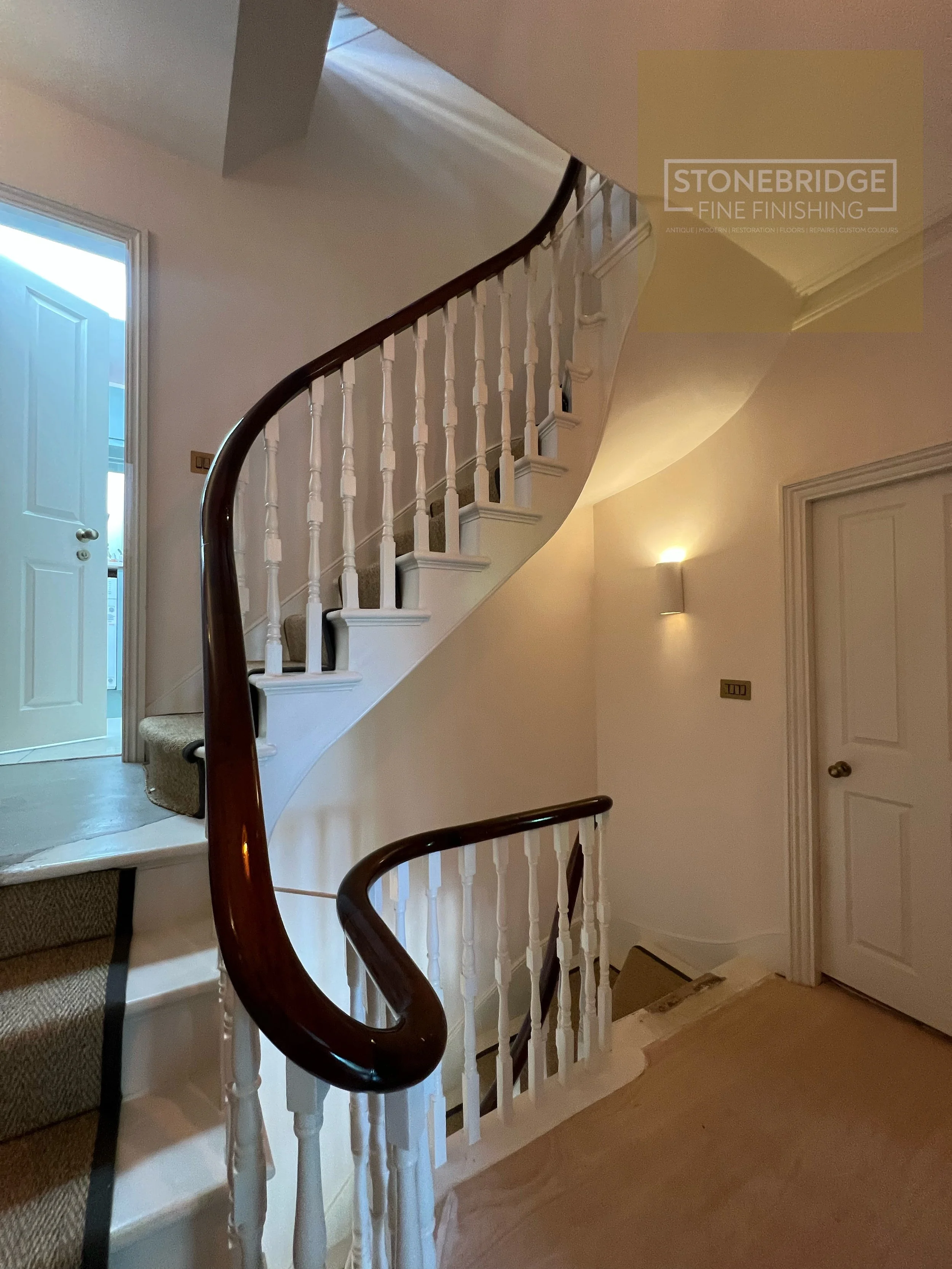 Interior view of a staircase with white balustrades and dark wooden handrails, inside a home with beige walls and carpeted stairs.