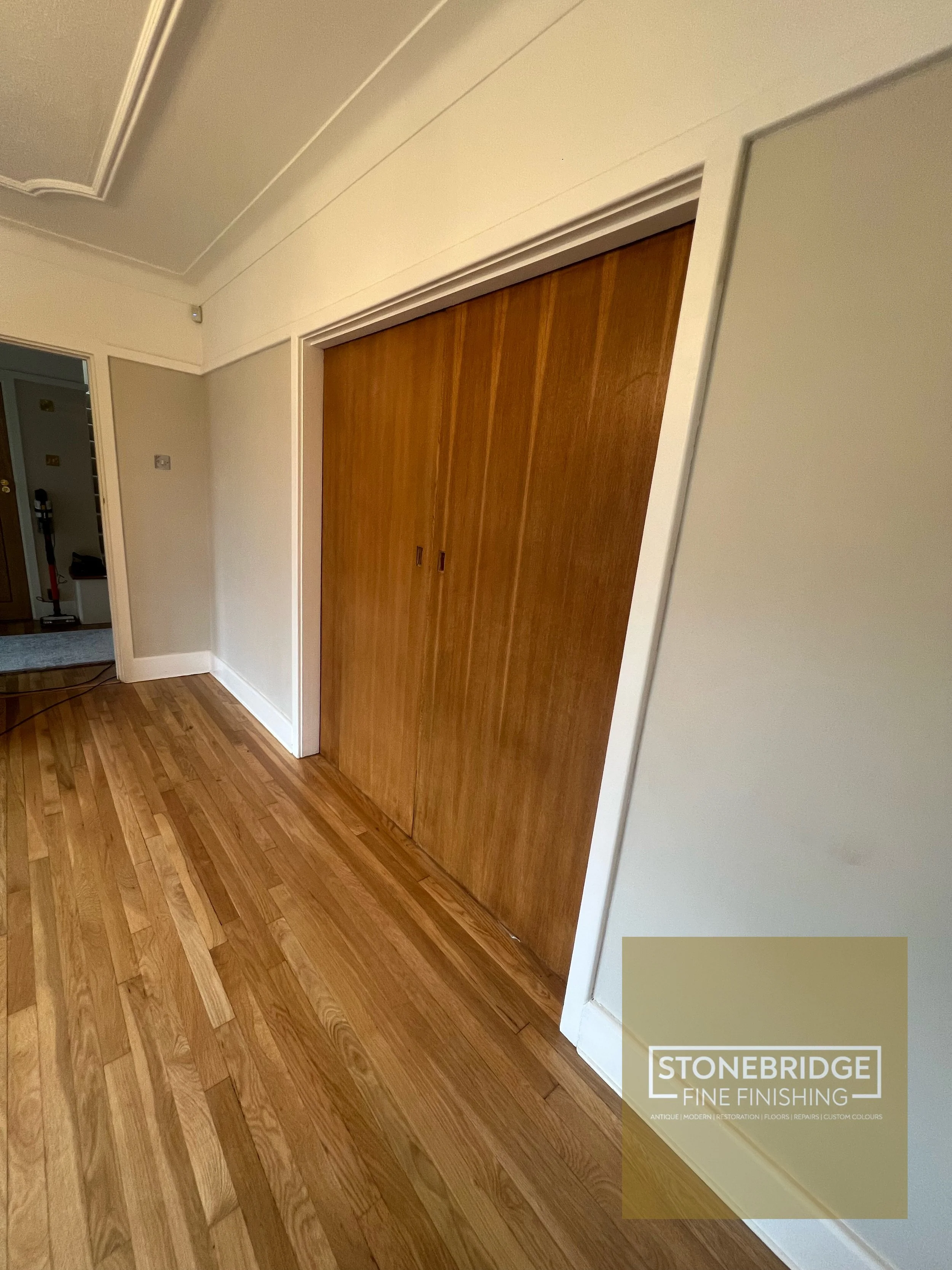 Photo of a wooden sliding closet door in a room with wooden flooring and beige walls. On the bottom right, there is a marketing overlay for Stonebridge Fine Finishing, highlighting services related to antique, modern, and restoration flooring, repair
