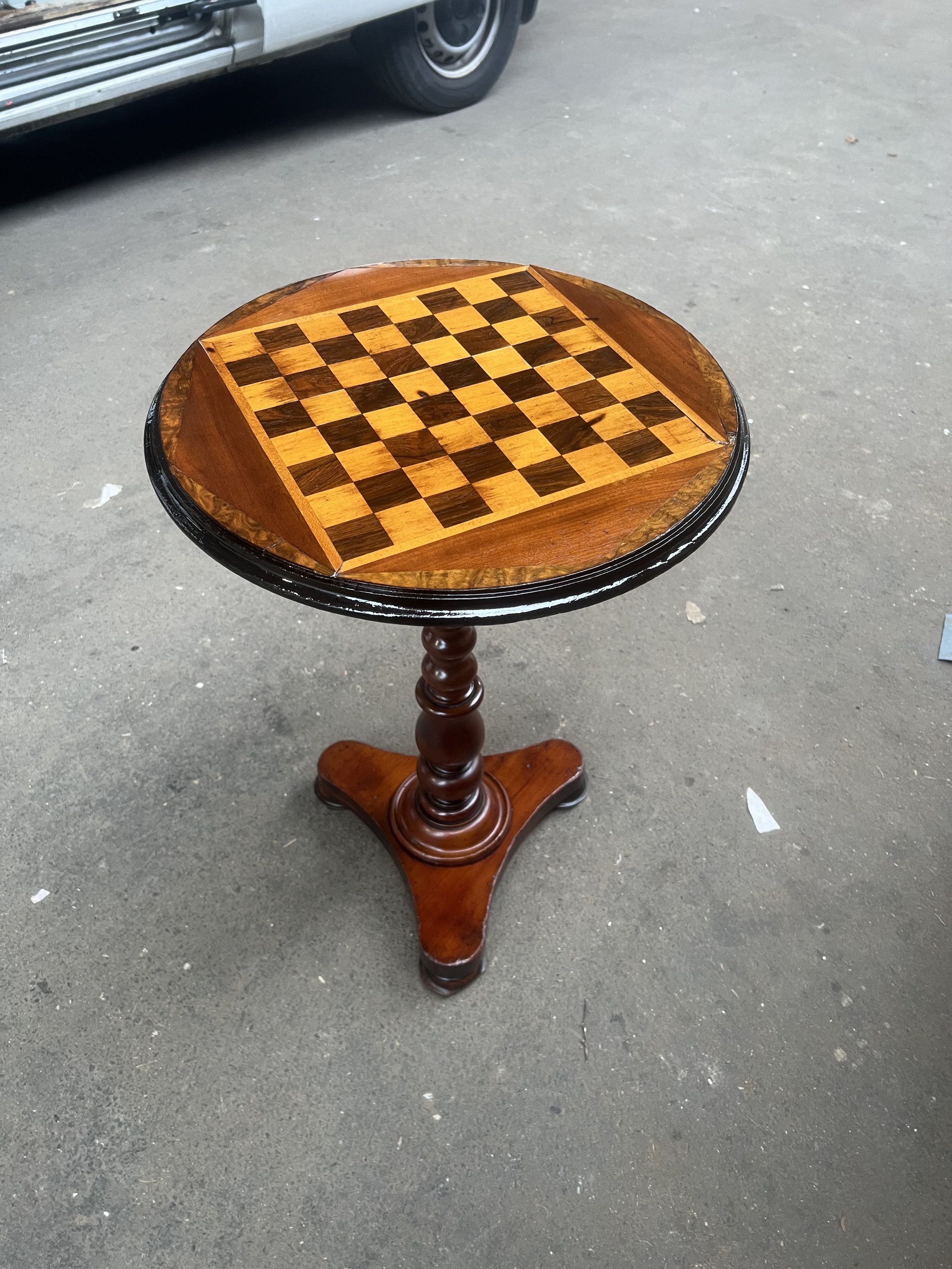 Round wooden table with a built-in chessboard on top, standing on a three-legged pedestal base.