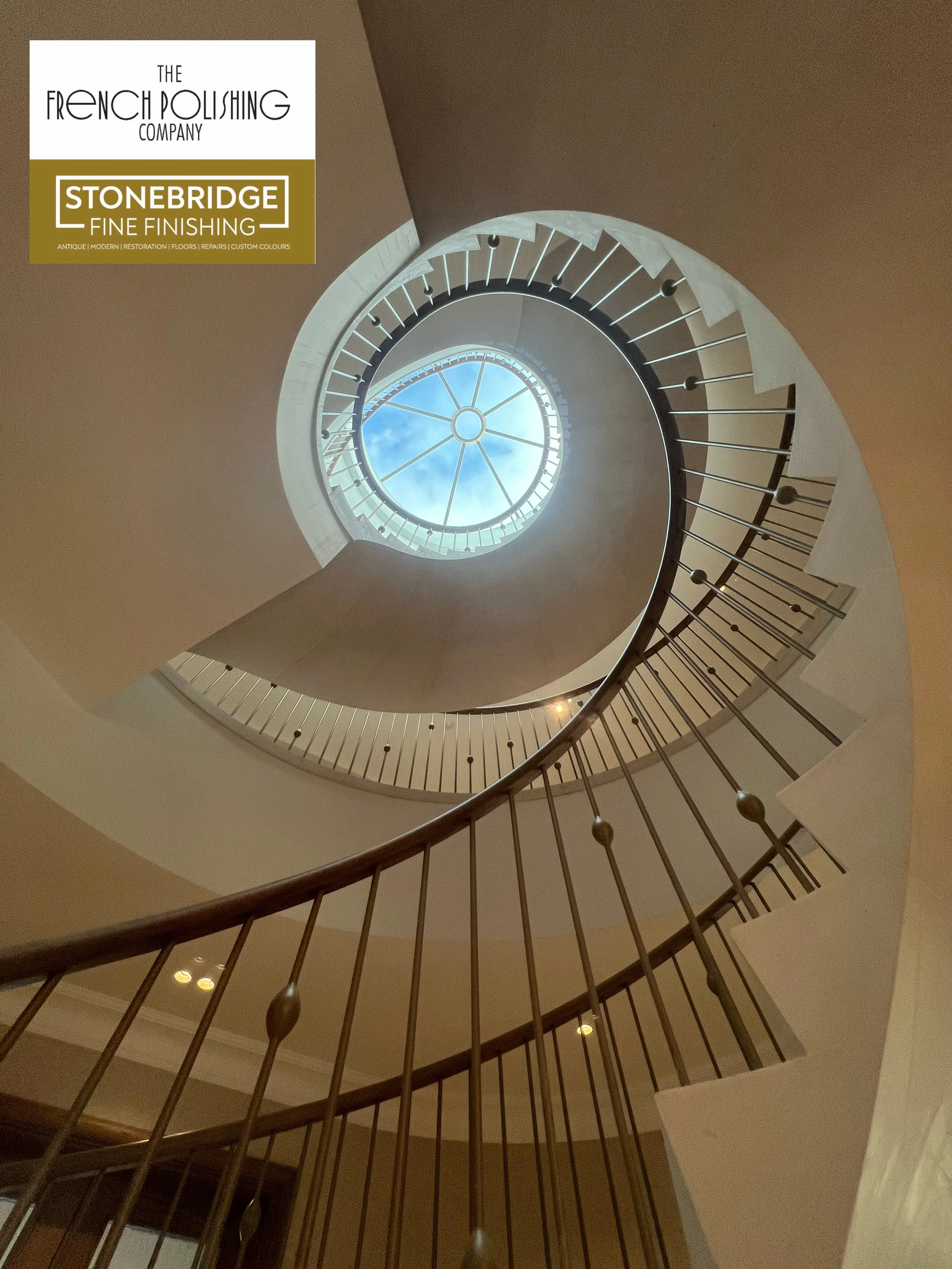 Spiral staircase with metal railing and ceiling skylight with clouds and blue sky visible.