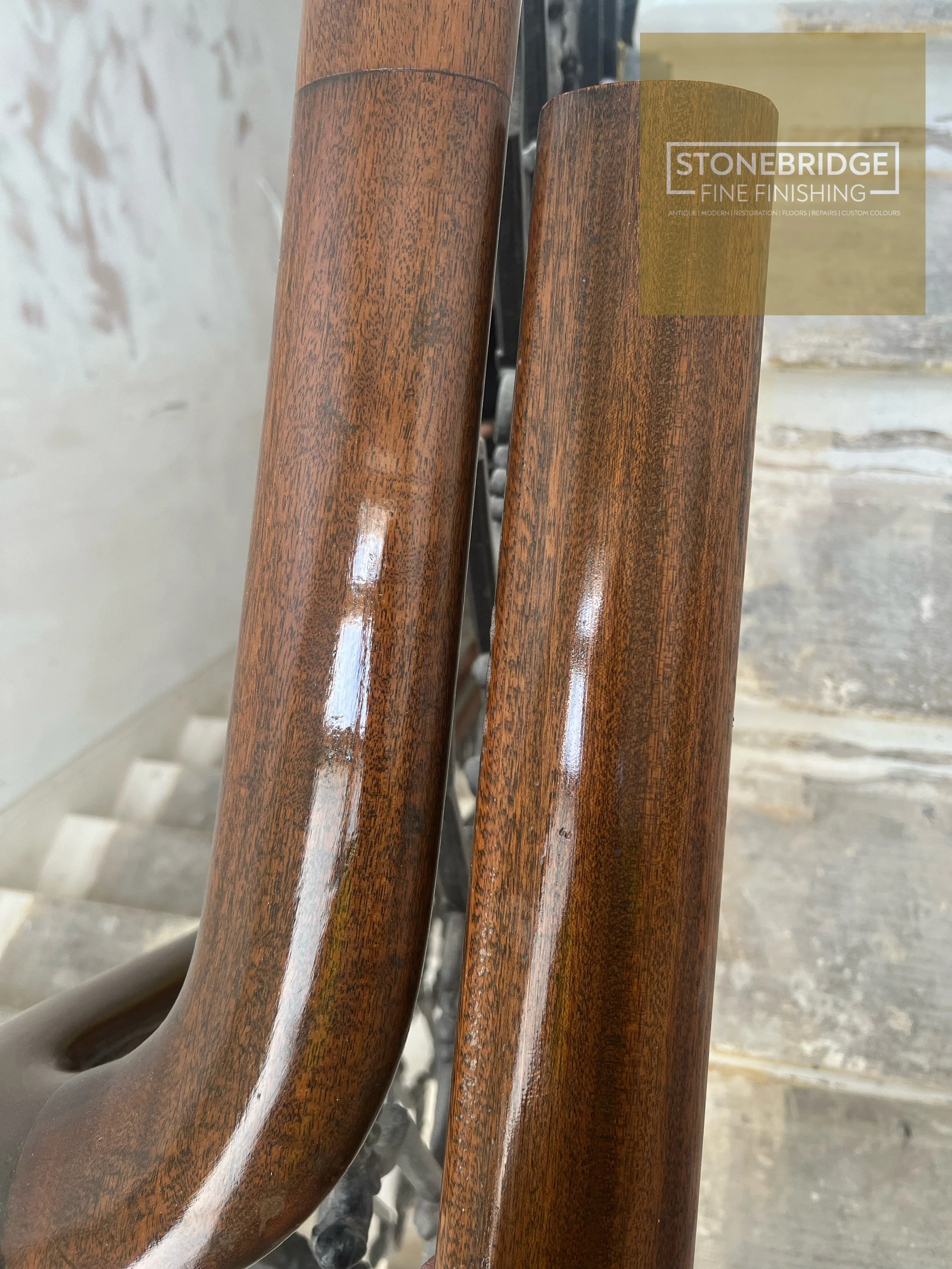 Close-up of three polished wooden chair legs with a background of stone and cement surfaces, and a logo overlay for Stonebridge Fine Finishing.