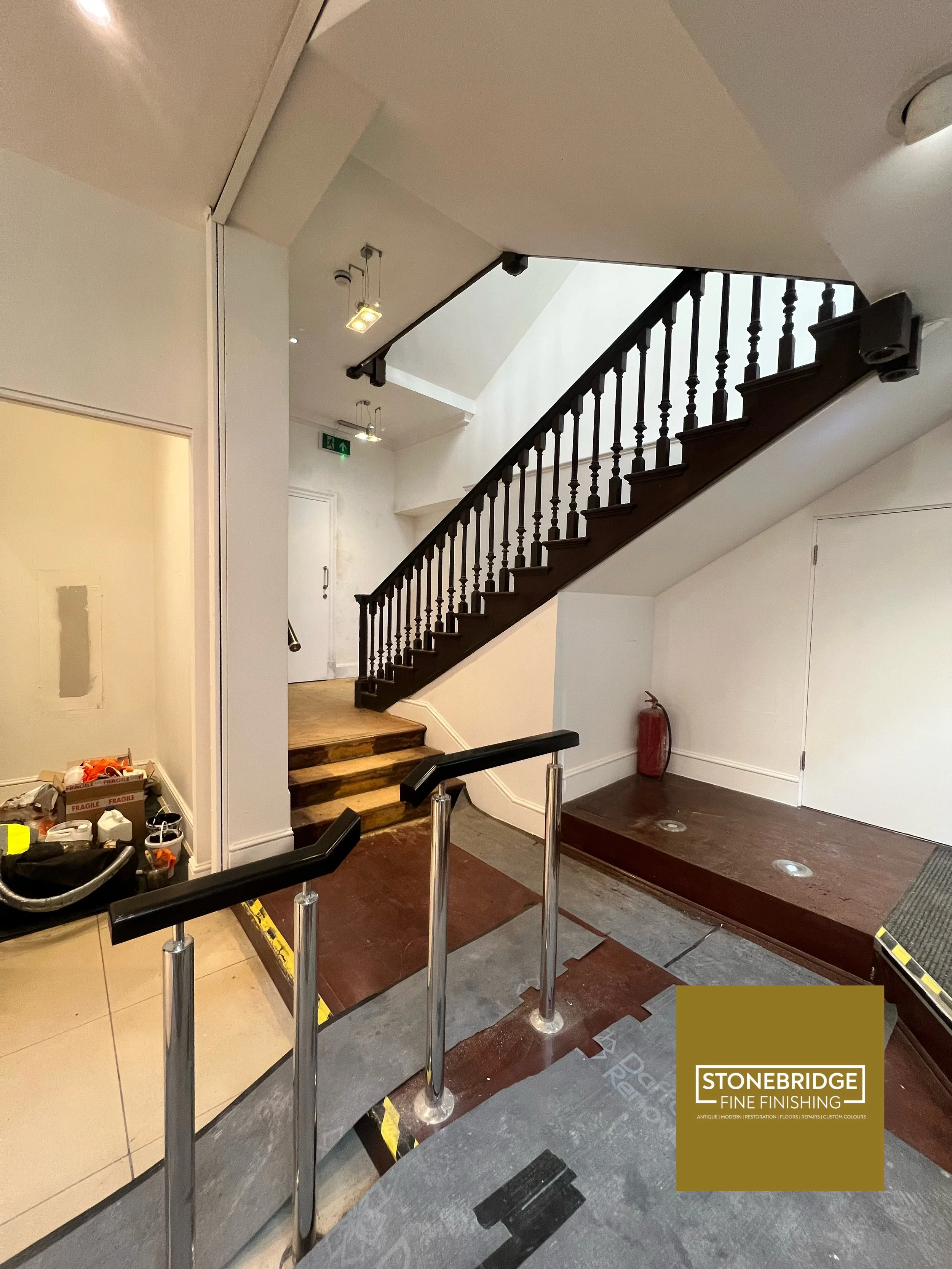 Interior space with stairs under renovation, partially installed flooring, tools, and a sign for Stonebridge Fine Finishing.