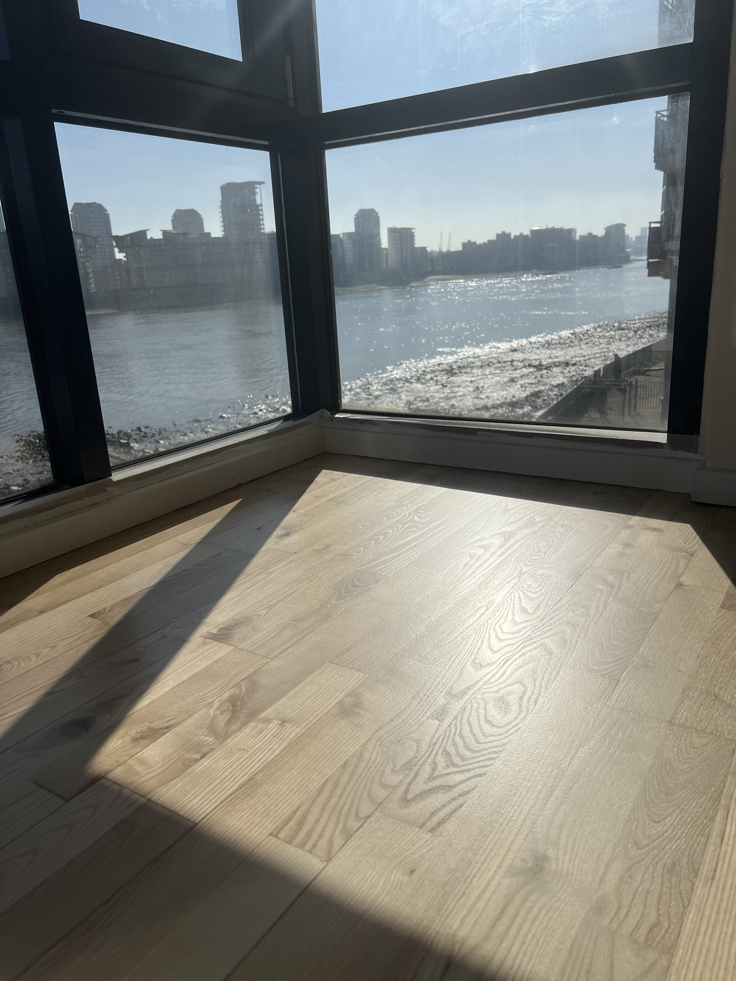Sunlit room with wooden floor and large windows showing city river view