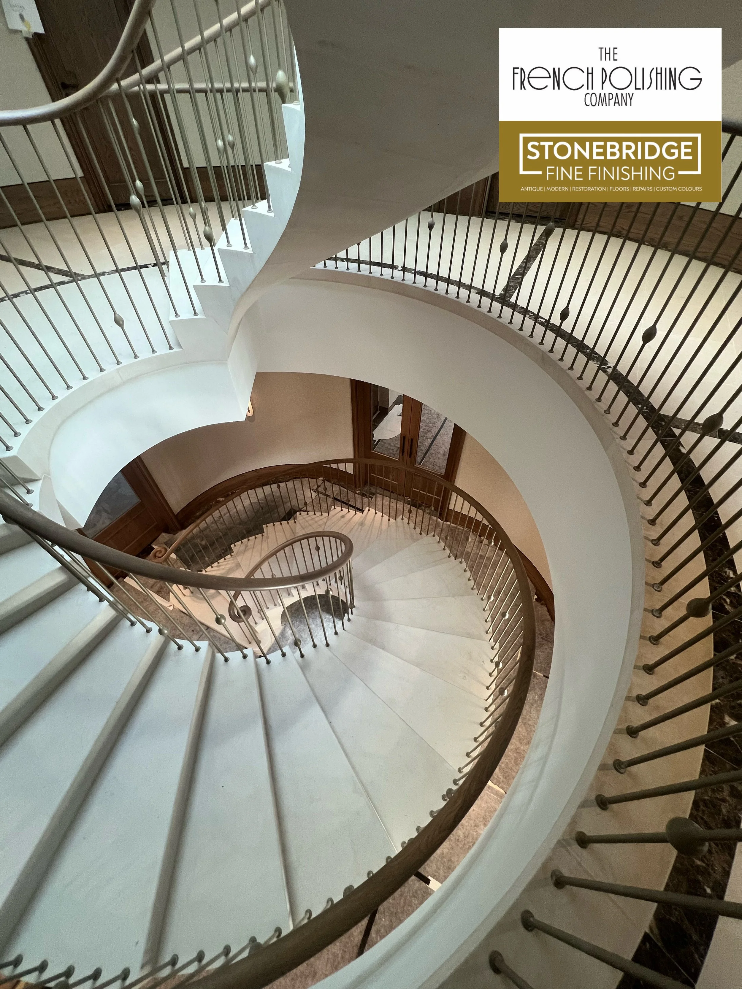 Spiral staircase with white steps, wooden handrail, and metal balusters, viewed from above in a multi-story interior