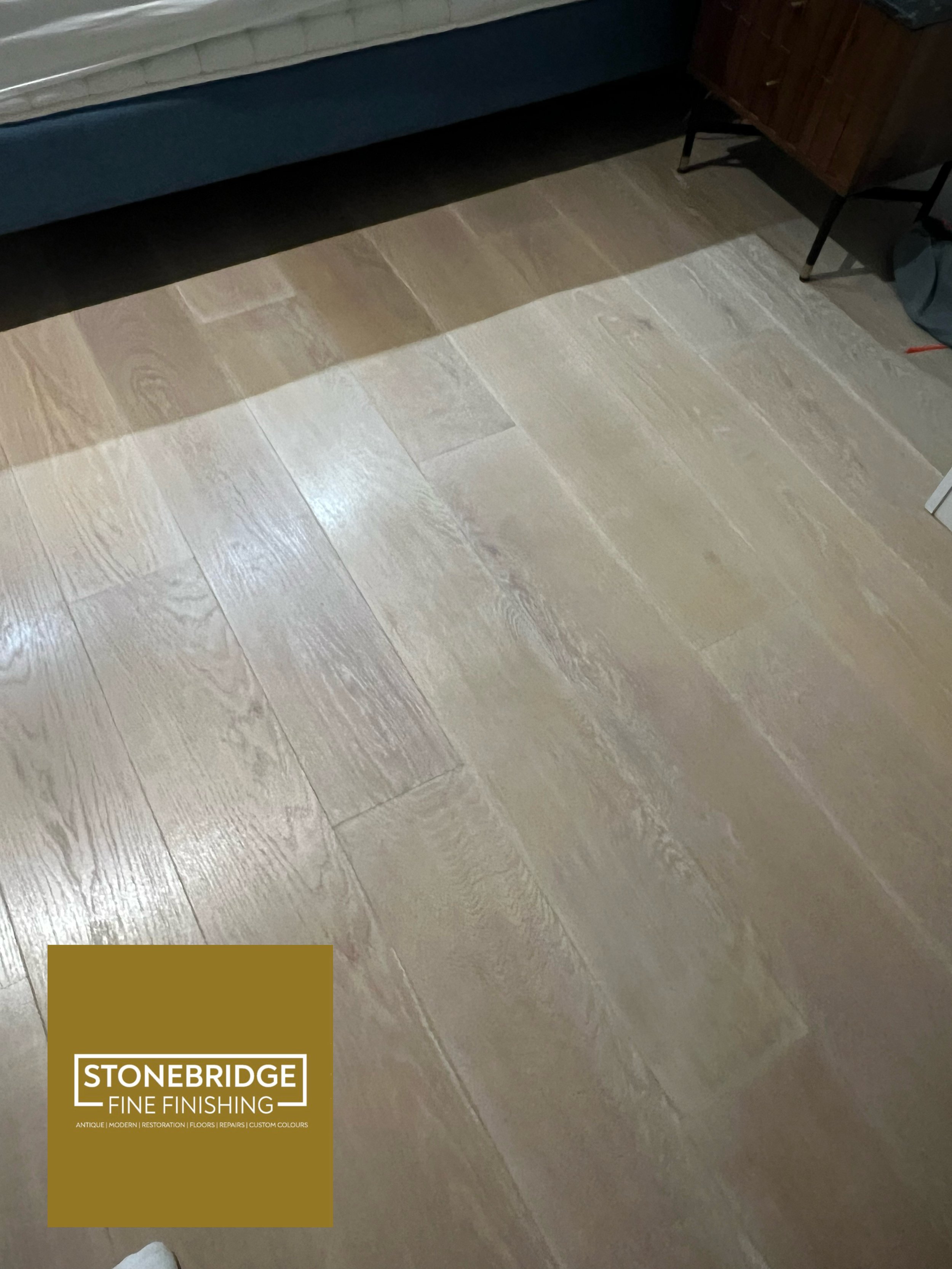 Wood flooring with a light, textured finish. In the lower left corner, there is a Stonebridge Fine Finishing logo in a gold box.