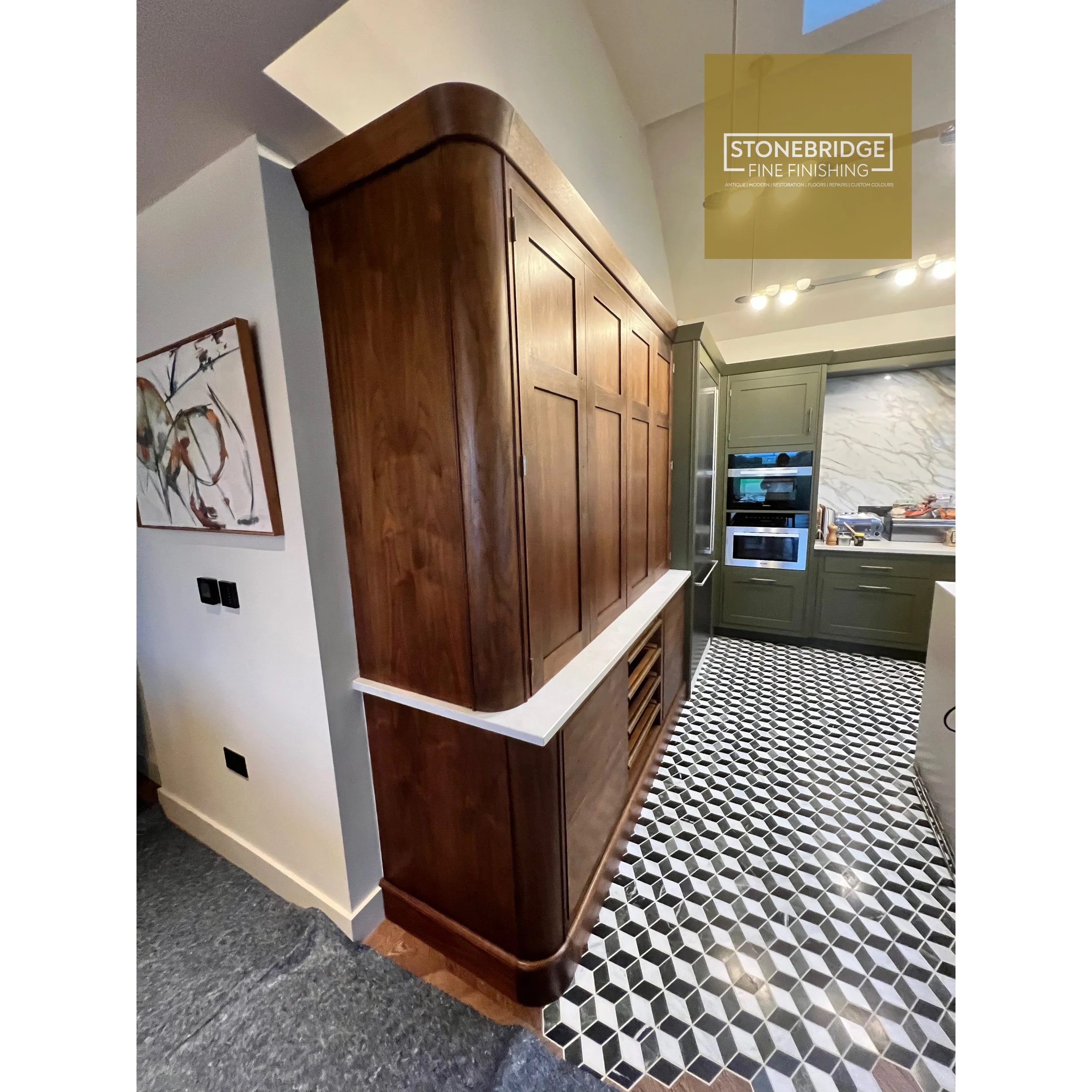 Interior of a home with a wooden cabinet, grey walls, abstract artwork, and black and white patterned tile flooring.
