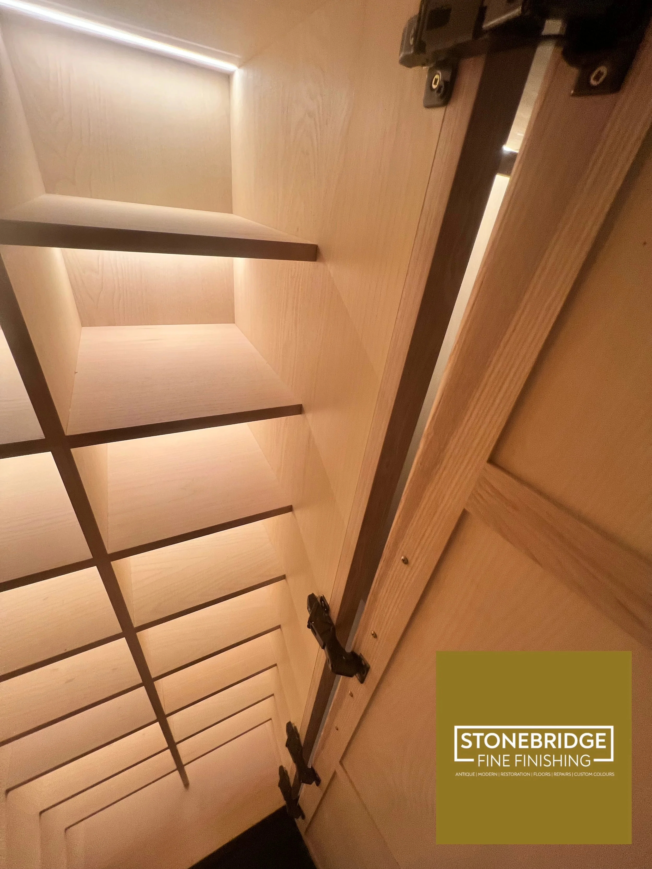 Interior view of a wooden cabinet with adjustable shelves, with a logo for Stonebridge Fine Finishing in the bottom right corner.