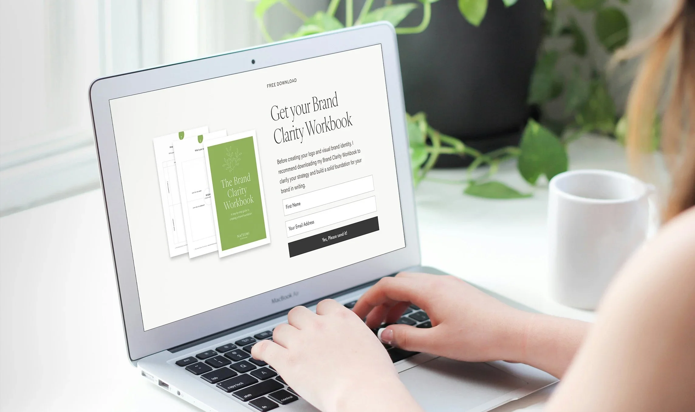 Laptop showing brand clarity workbook download form with plants and mug