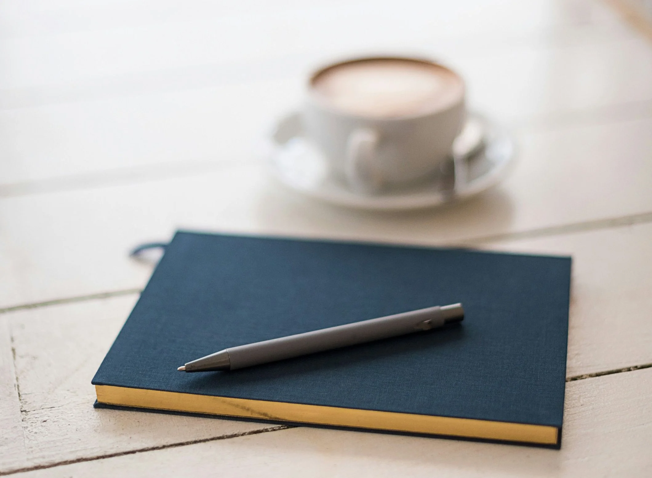 Closed blue notebook with gray pen and white coffee cup