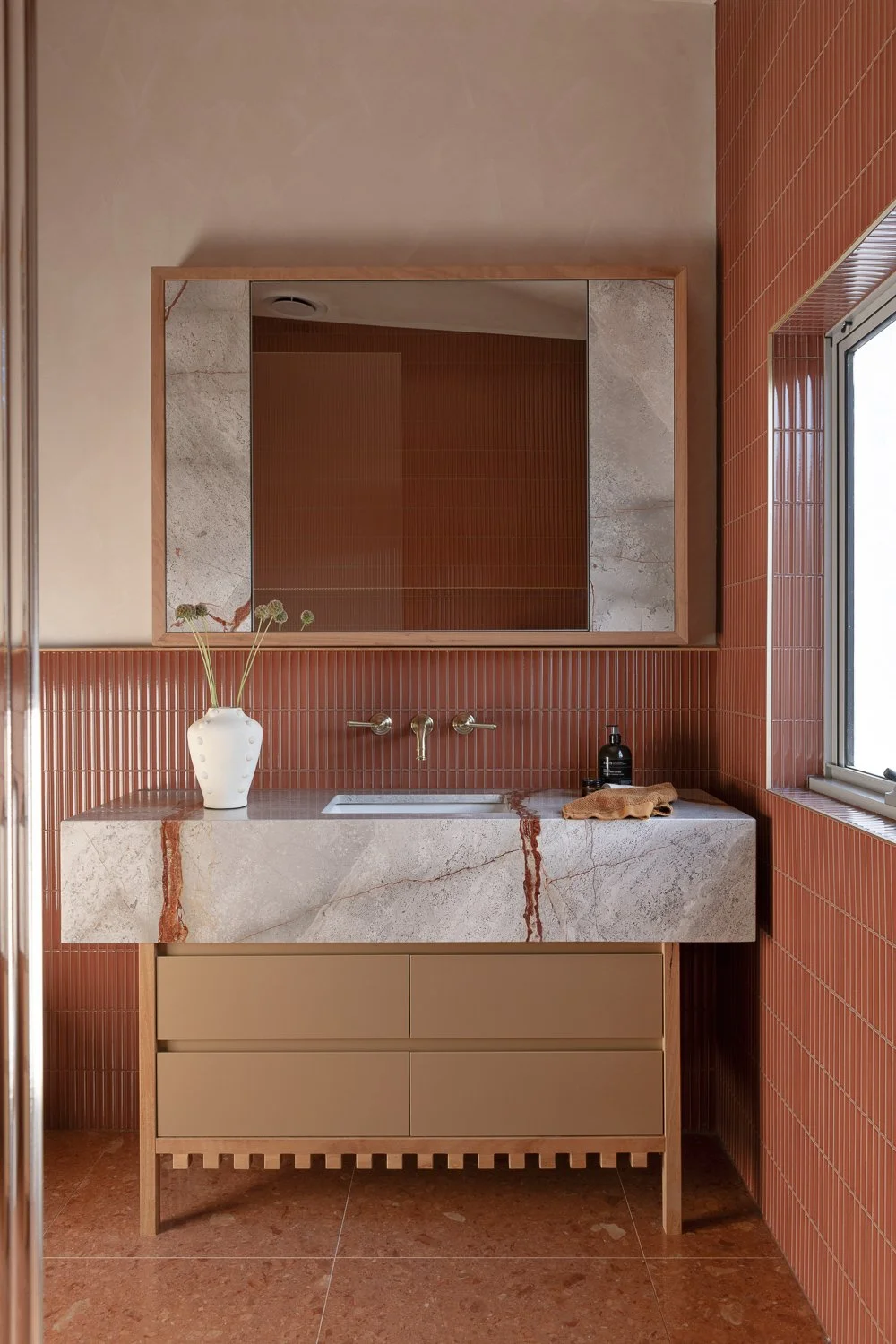 Brighton House — Inside, materials are warm and tactile. Terracotta tones, blackbutt timber and rendered surfaces create a grounded interior, while joinery is expressed as furniture.