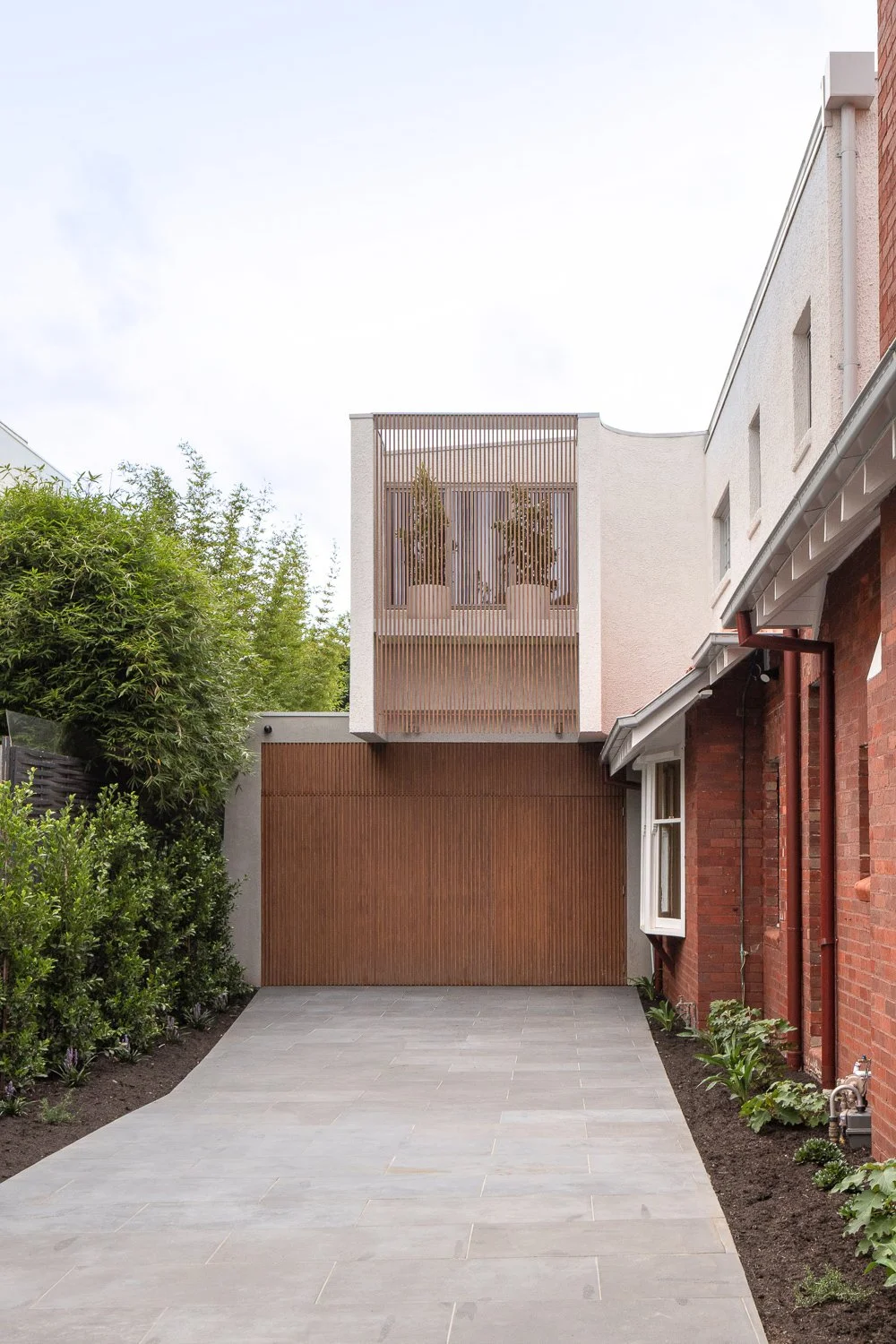 Brighton House- master ensuite featuring a secluded garden that brings in soft, dappled light. Timber batten screens and lush pot-plant greenery create a layered, tranquil atmosphere.