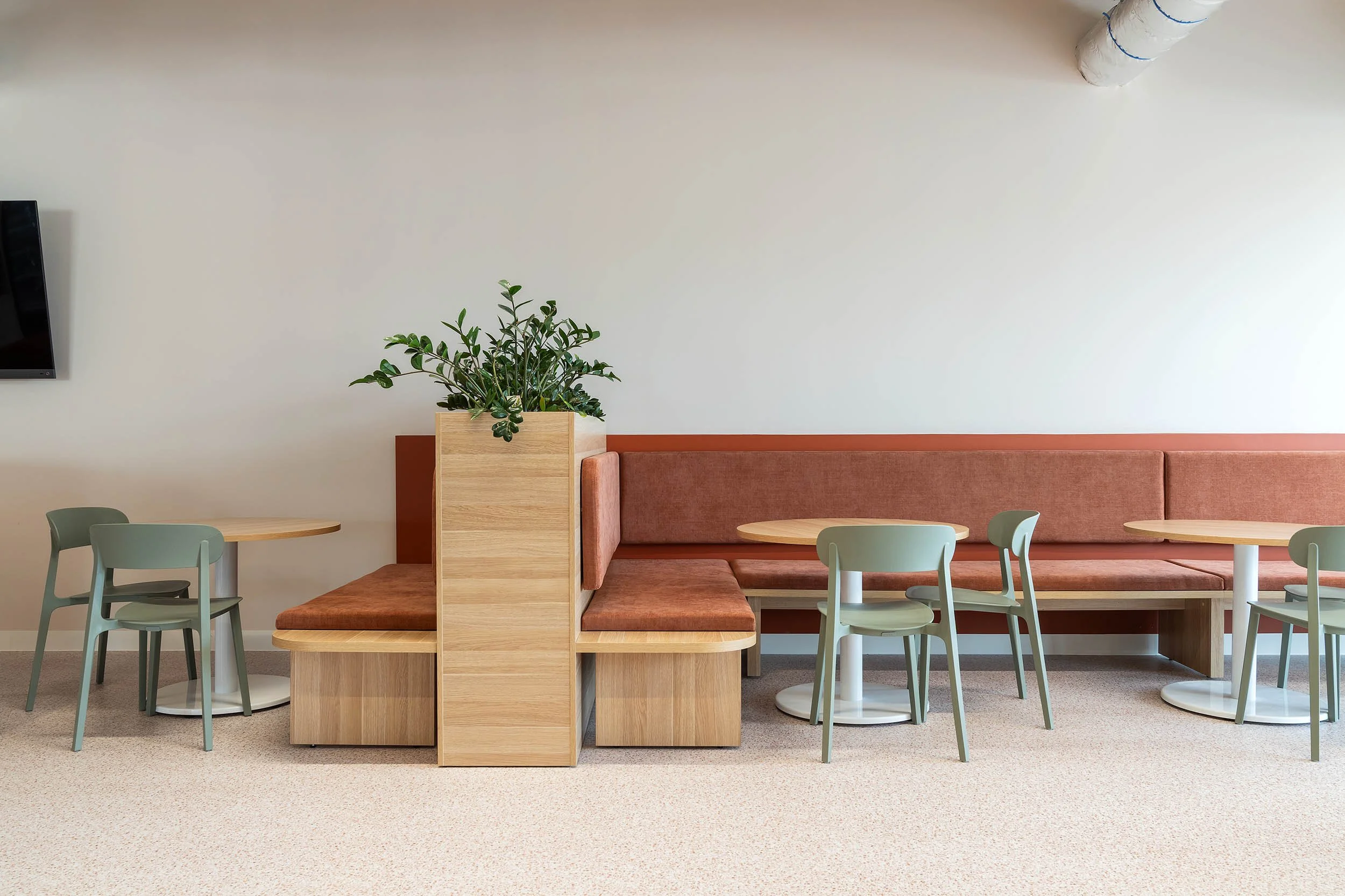 Minimalist office lounge area featuring a long, low wooden bench seat against a stark white wall.