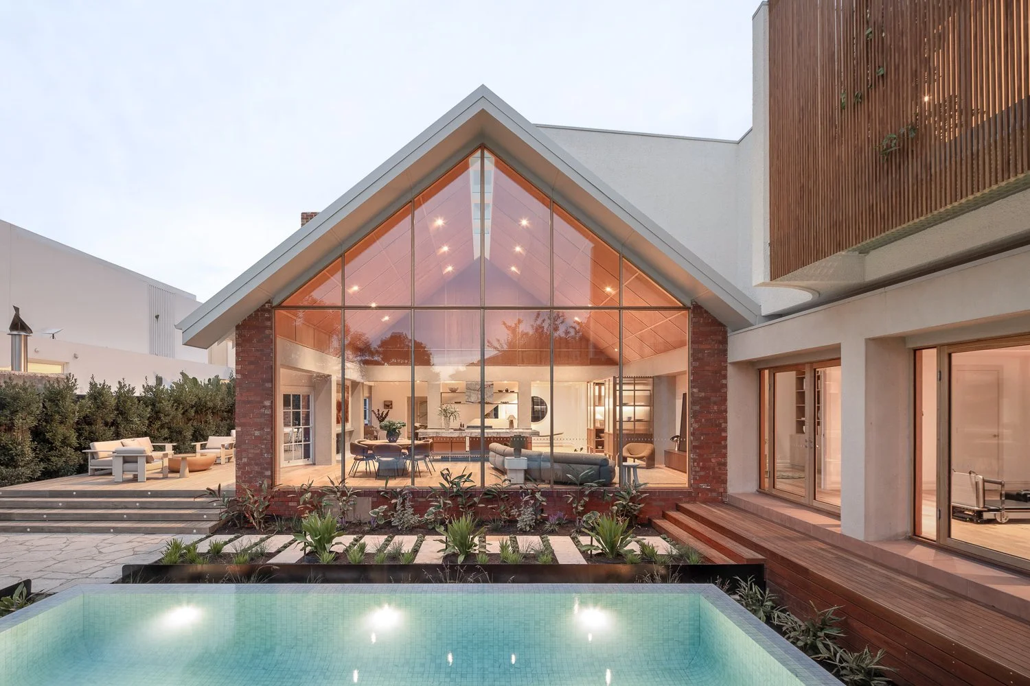 Brighton House — the master suite features a secluded garden that filters soft, dappled light through timber batten screens and lush pot-plant greenery, creating a layered and tranquil atmosphere. The south-facing living room opens directly onto the 