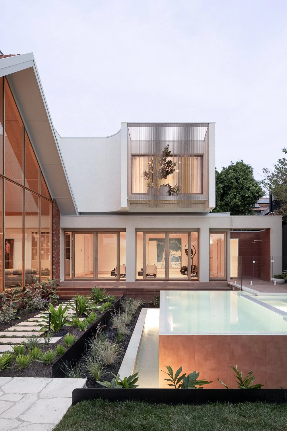 Brighton House — The new master suite sits above the garage and wellness area, integrated through a softened junction and a textured white render. A cantilevered balcony extends from the bedroom, designed as a small planted garden. A fine louvred scr