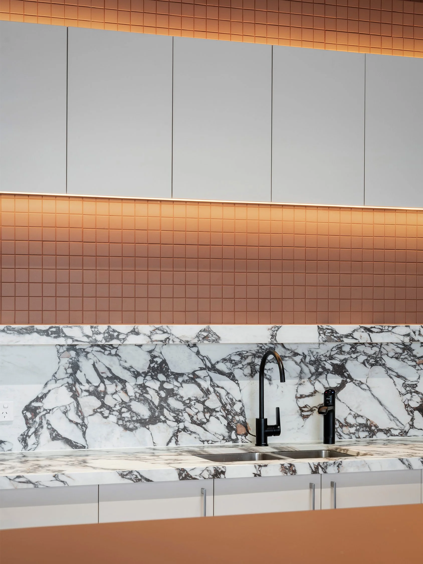 Close-up of a modern office kitchen counter with a patterned gray marble backsplash and overhead wooden cabinetry.