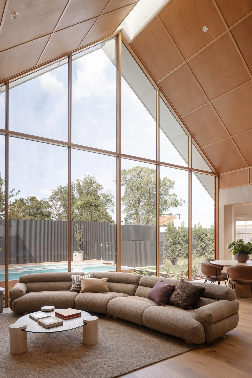 Brighton House — The south-facing living room opens directly onto the pool area, while a cathedral ceiling with a central skylight brings natural light into the space throughout the day.