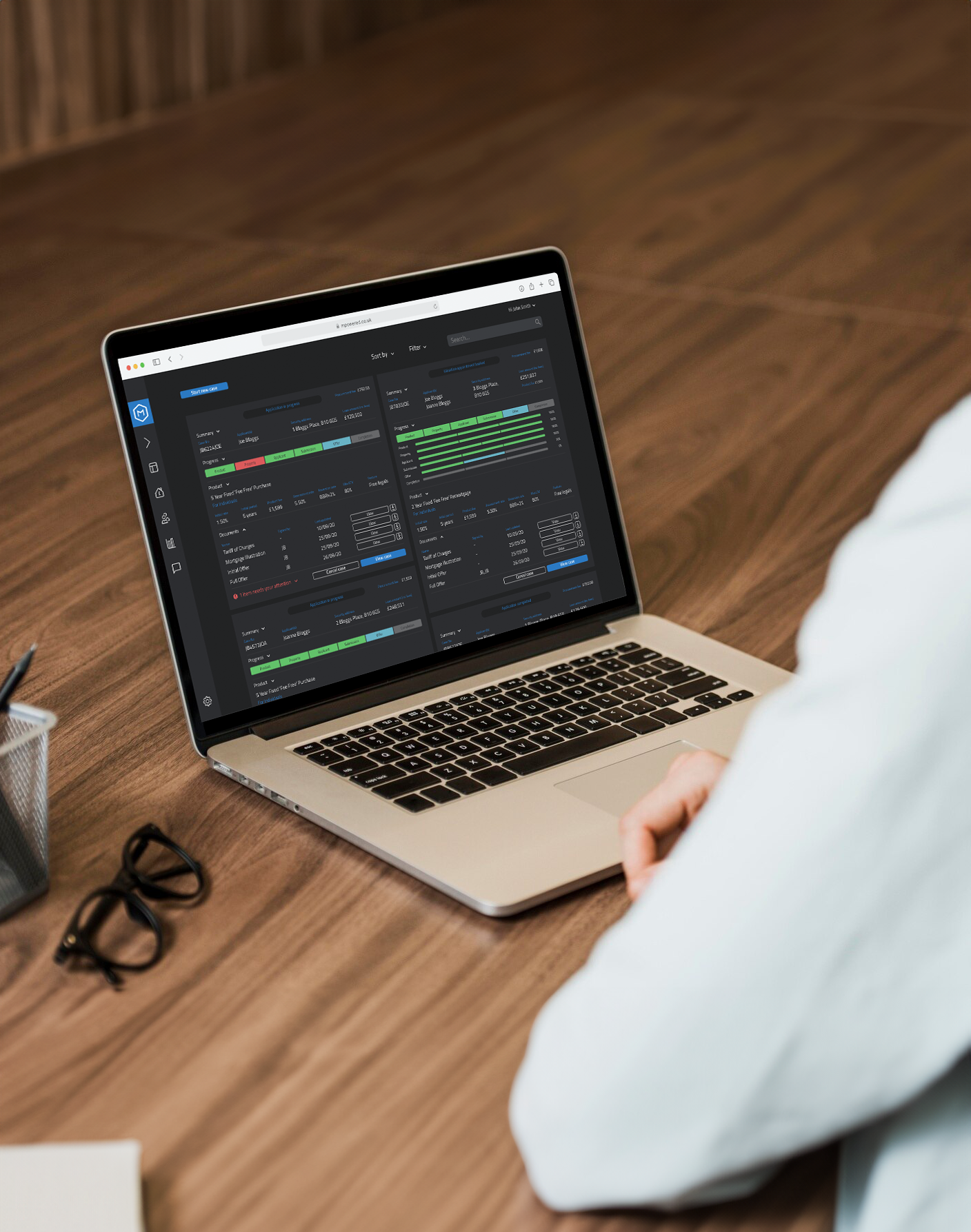 Person working on a laptop displaying data analytics and graphs on a dark background, on a wooden desk with glasses and writing utensils nearby.