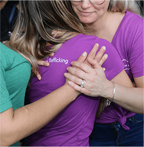 Two people in colorful t-shirts embracing closely, focusing on their hands and arms, with partial text visible on one shirt.