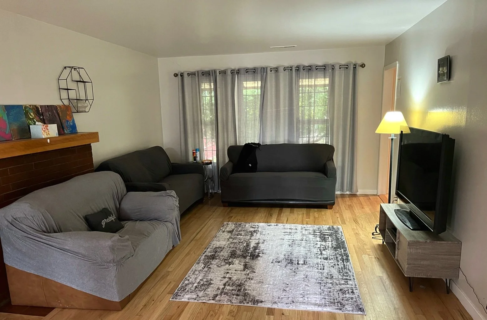 Room of a MCYP shelter home featuring couches, a tv, a rug, and curtains in front of a large window