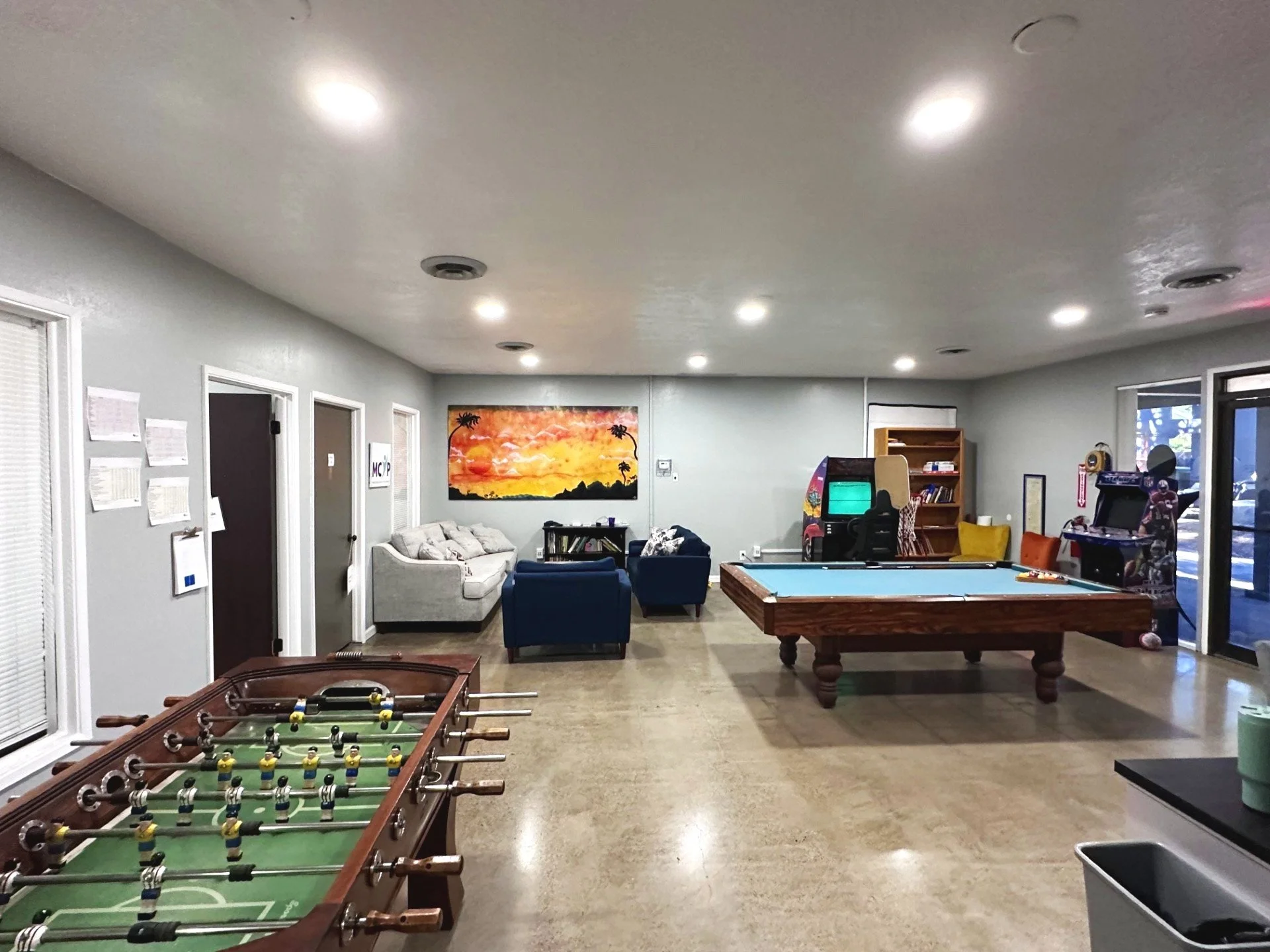 Large room with couches, ping-pong table, foosball table, art on walls, and Halloween-decoration skeleton sitting in chair