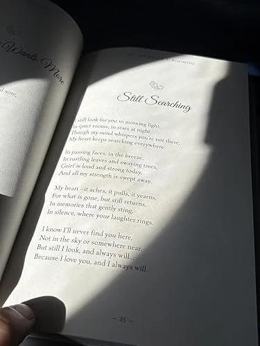 Open book with poem titled "Still Searching" illuminated by sunlight, with a person's finger holding the page.