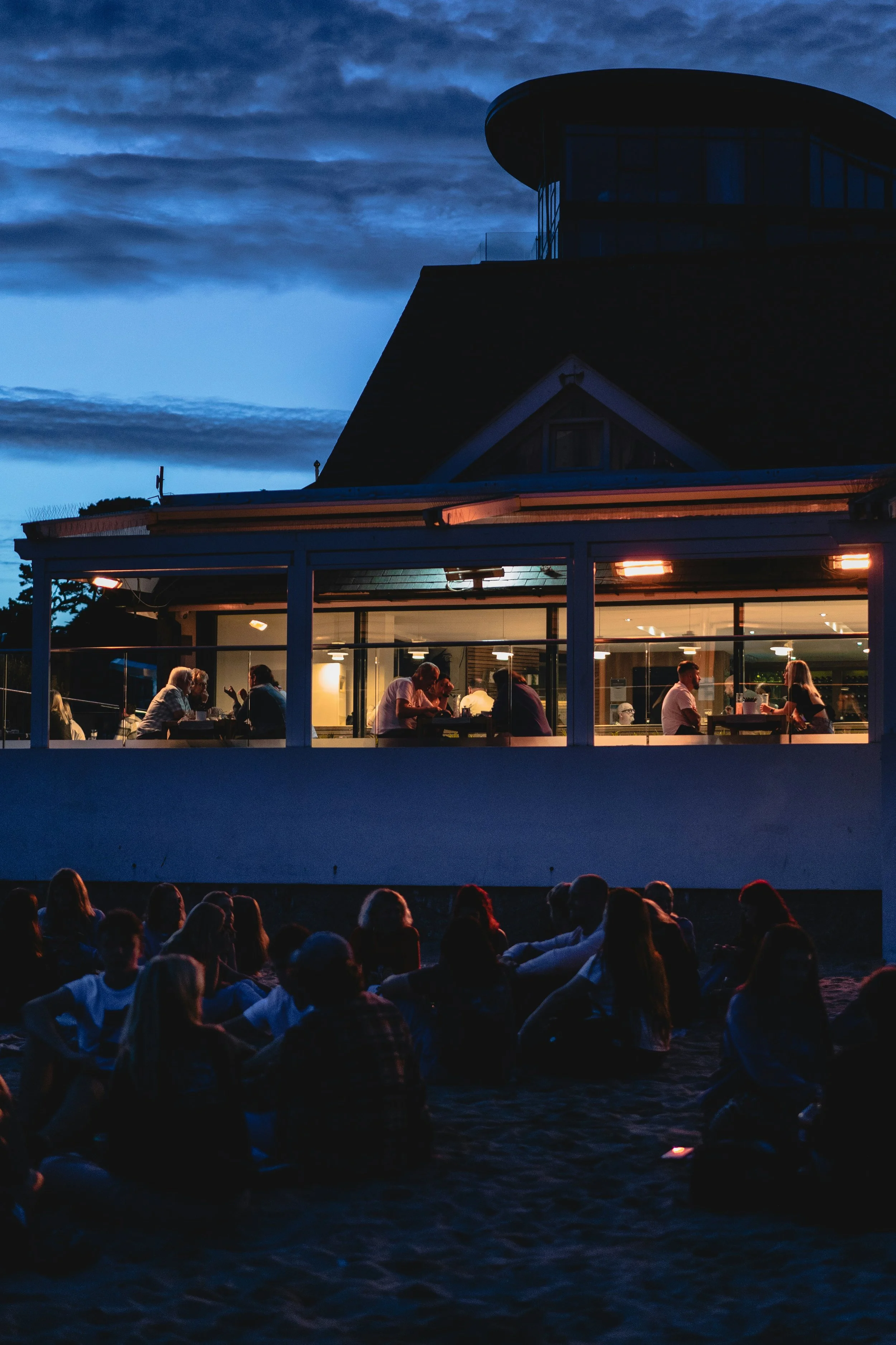 People sit on the outside patio of Gylly Beach Cafe at night enjoying a drink and a meal with friends