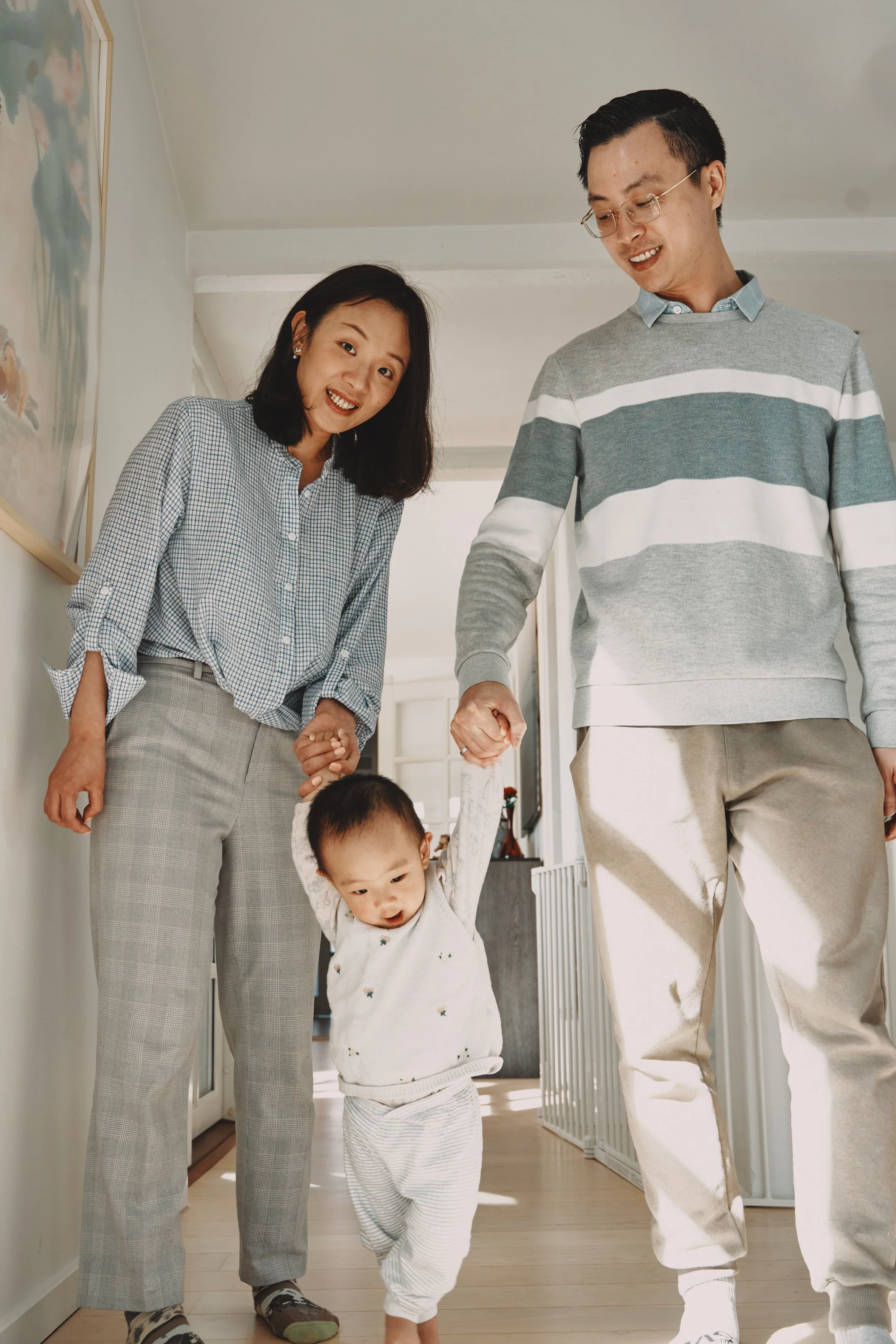 A family in a kitchen with a father holding a young child who is touching a lamp, while the mother smiles and guides the child's hand.