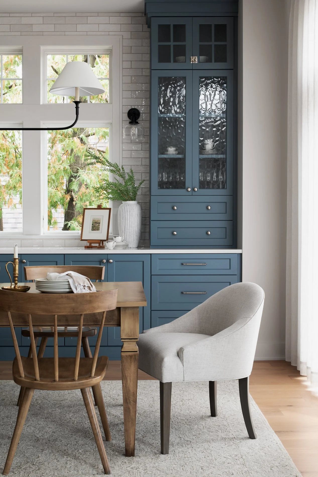 dining room with muddy blue cabinets, classic wood table and chairs, upholstered head chairs, white tile backsplash, white drapery